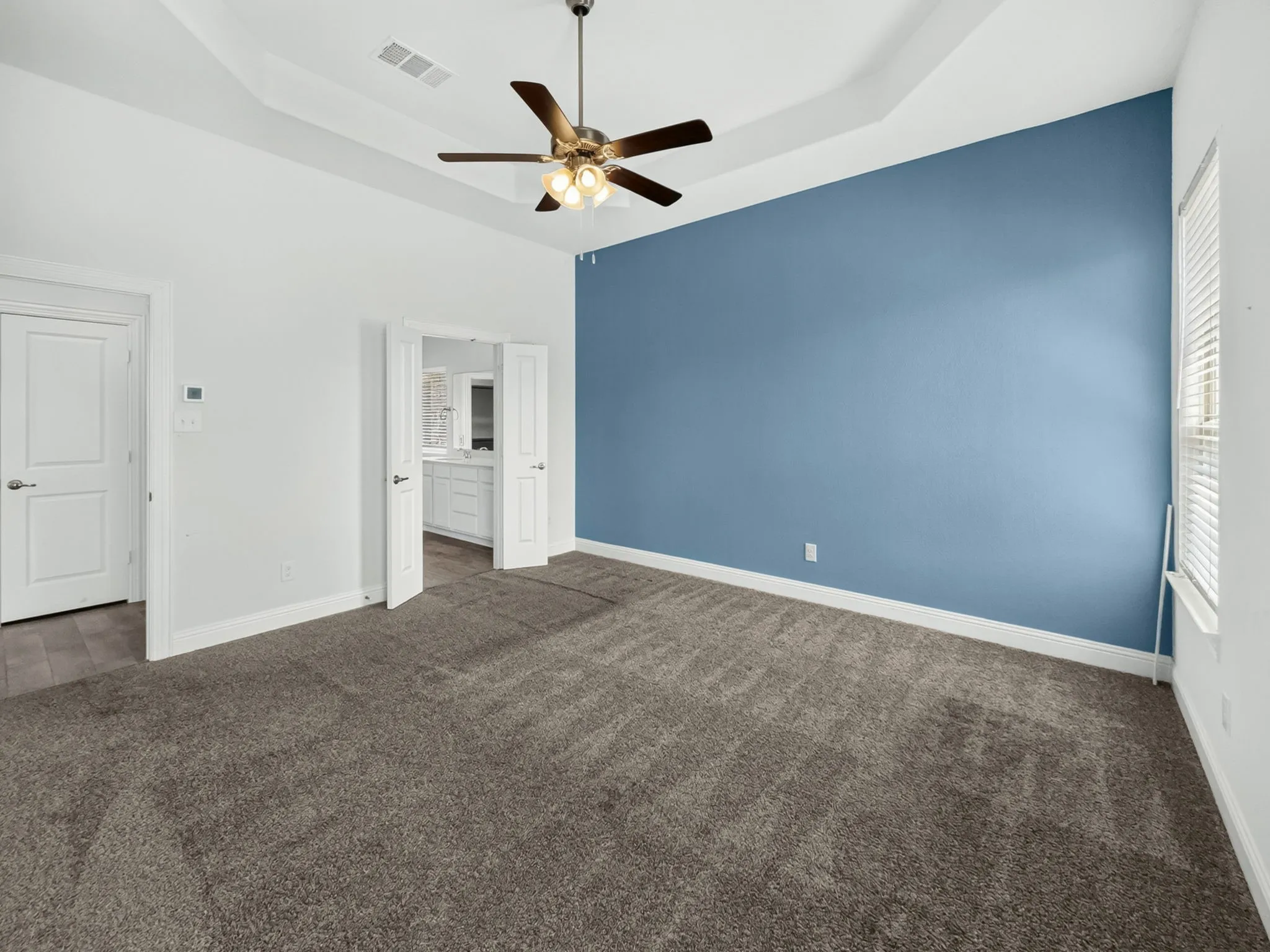Spacious room featuring tray ceiling, ceiling fan with lighting, contrasting accent wall, plush carpet, and white paneled doors