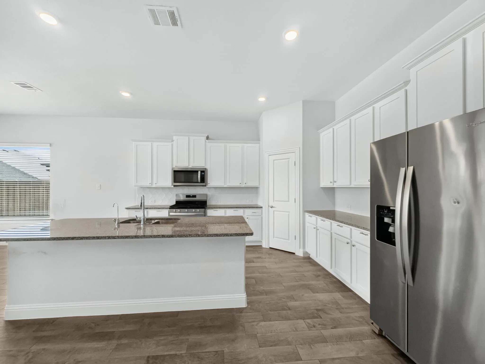 Kitchen featuring a central island with an undermount sink, white cabinetry, stainless steel appliances, speckled countertops, and wood-finish flooring
