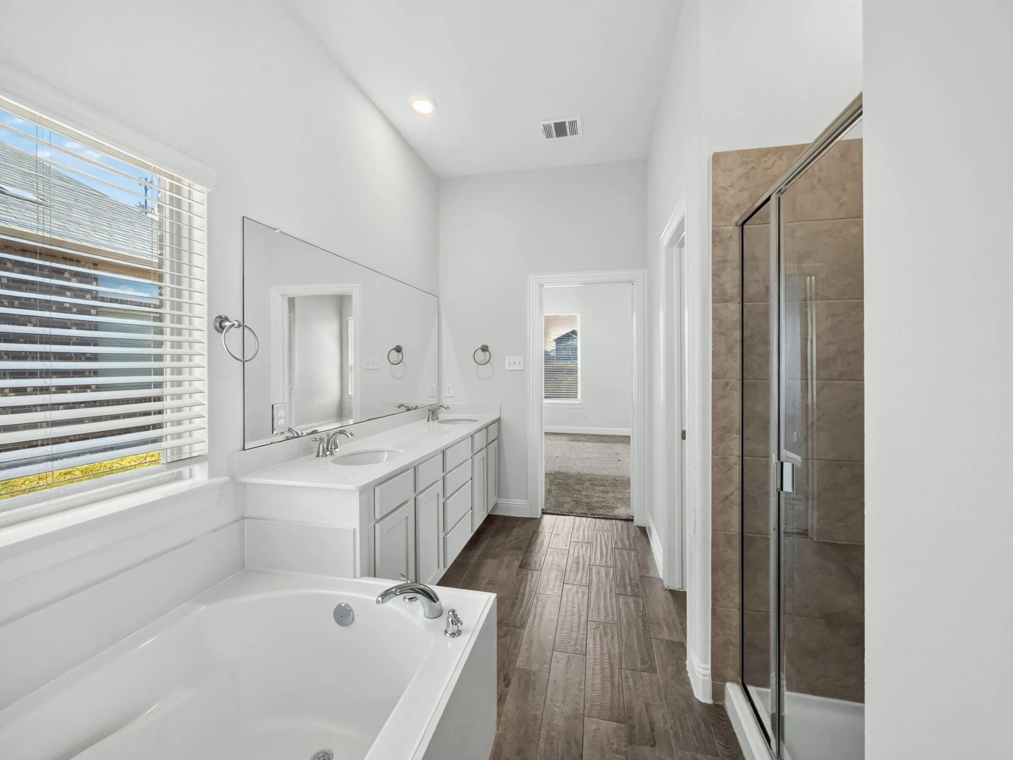 Bathroom featuring a double vanity with undermount sinks, a soaking tub, a tiled shower with a glass enclosure, and wood-finish flooring