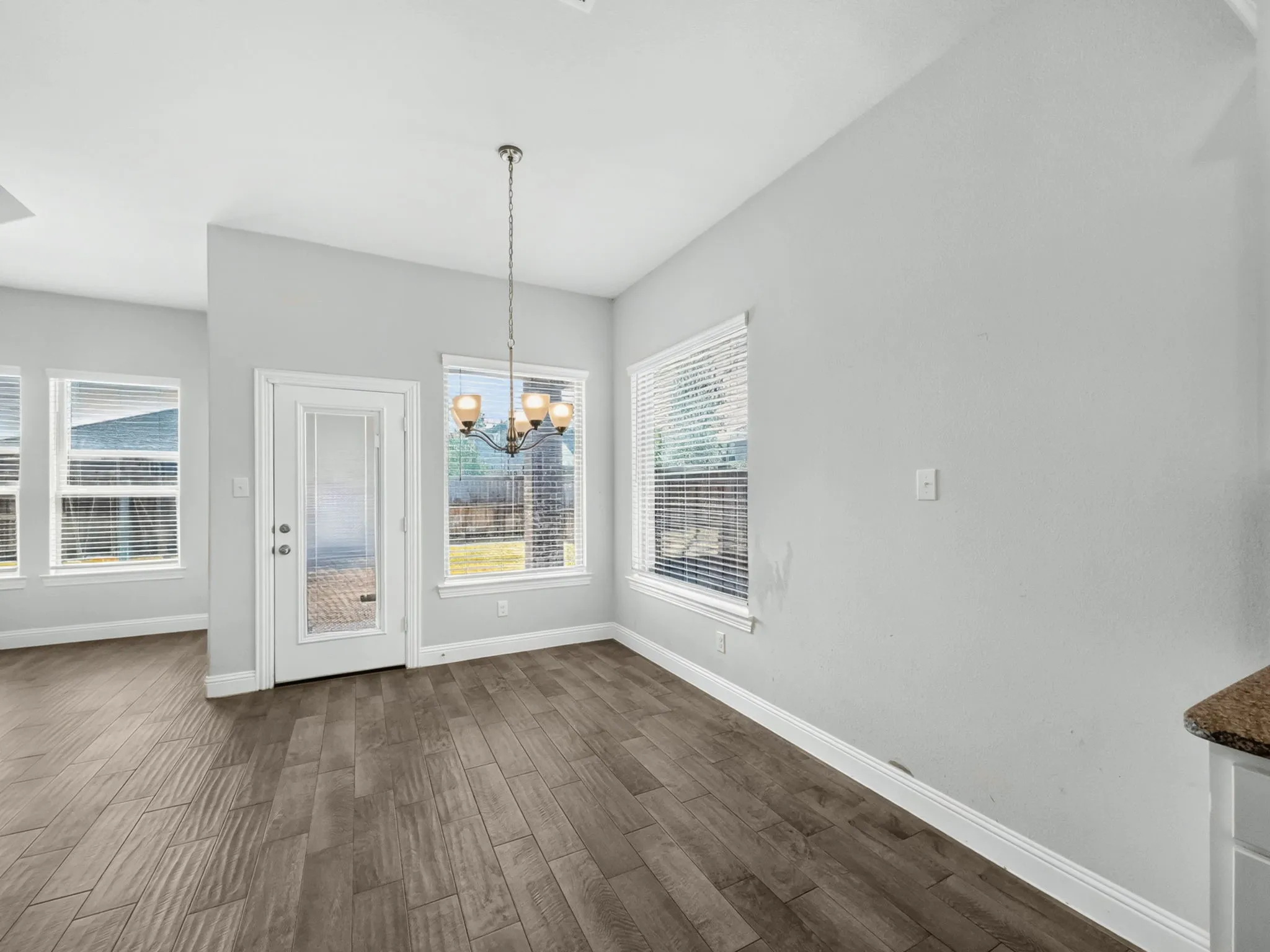 Dining area with wood-finish flooring, multiple windows, a glass-panel door, and a decorative chandelier