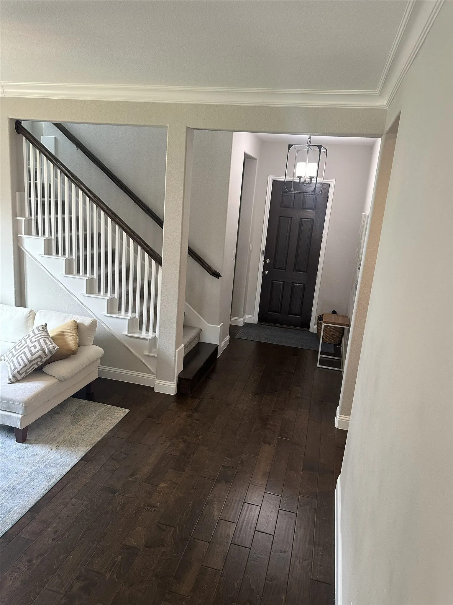 Hardwood flooring throughout the entry, staircase with white balusters and dark wood handrail, and a dark paneled front door with overhead lantern-style lighting