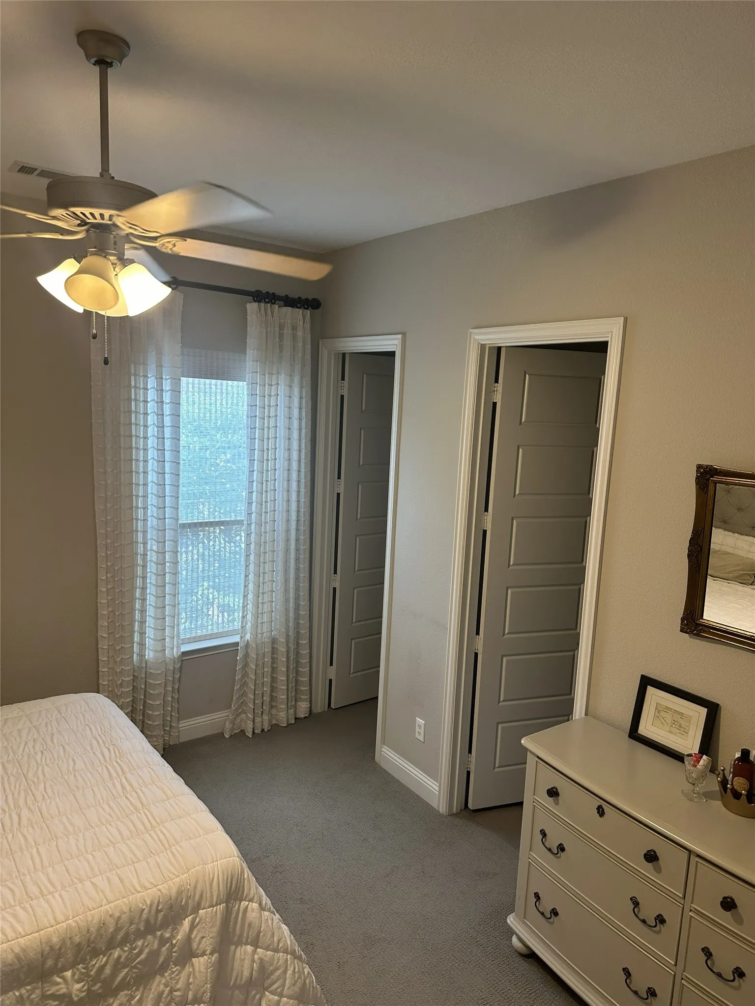 Ceiling fan with integrated lighting, window with light-filtering curtains, two panel doors with trim, and neutral wall paint