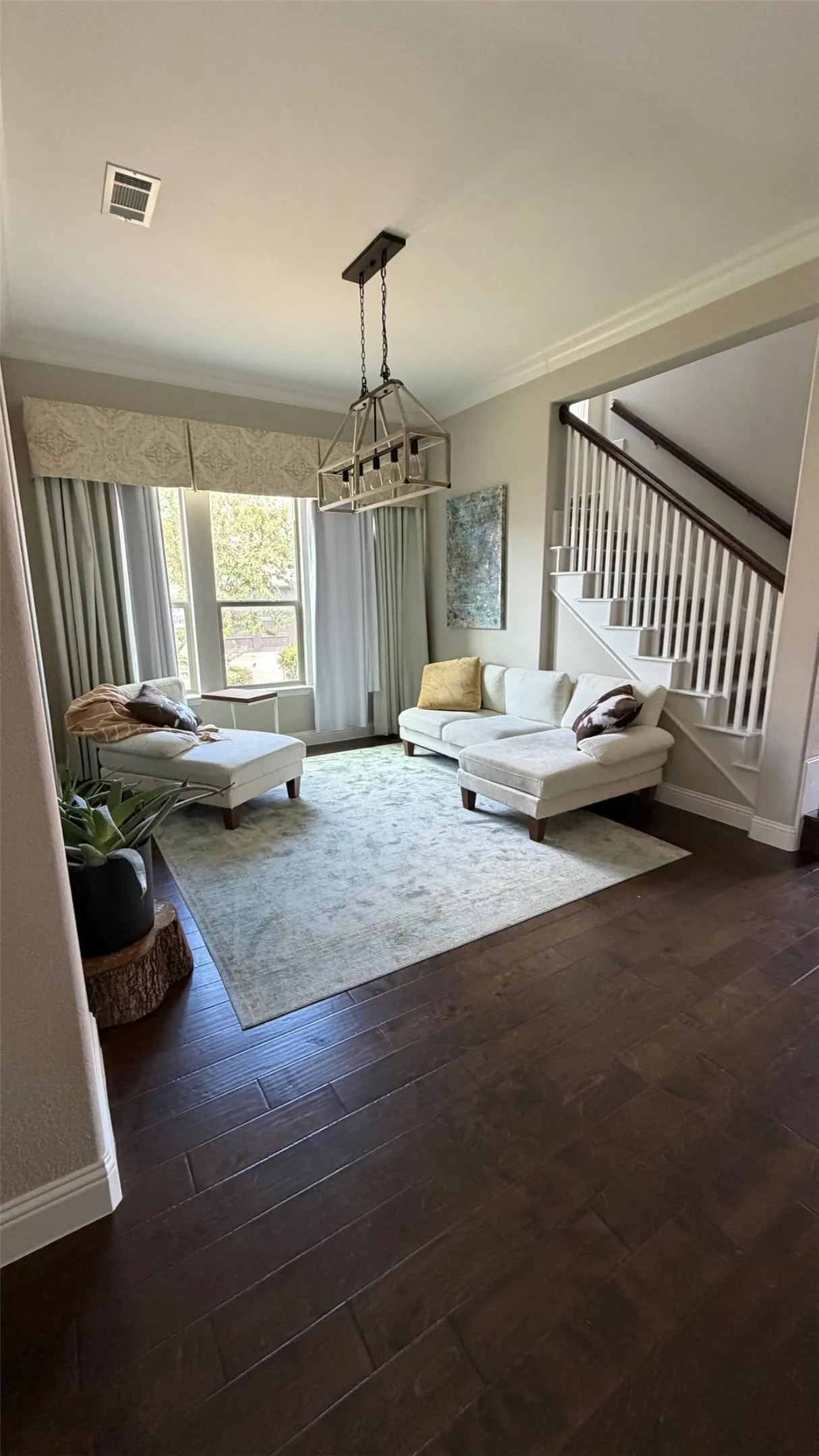 Dark wood-finish flooring, a multi-pane window, a rustic-style rectangular chandelier, a white staircase with dark wood handrails, and crown molding
