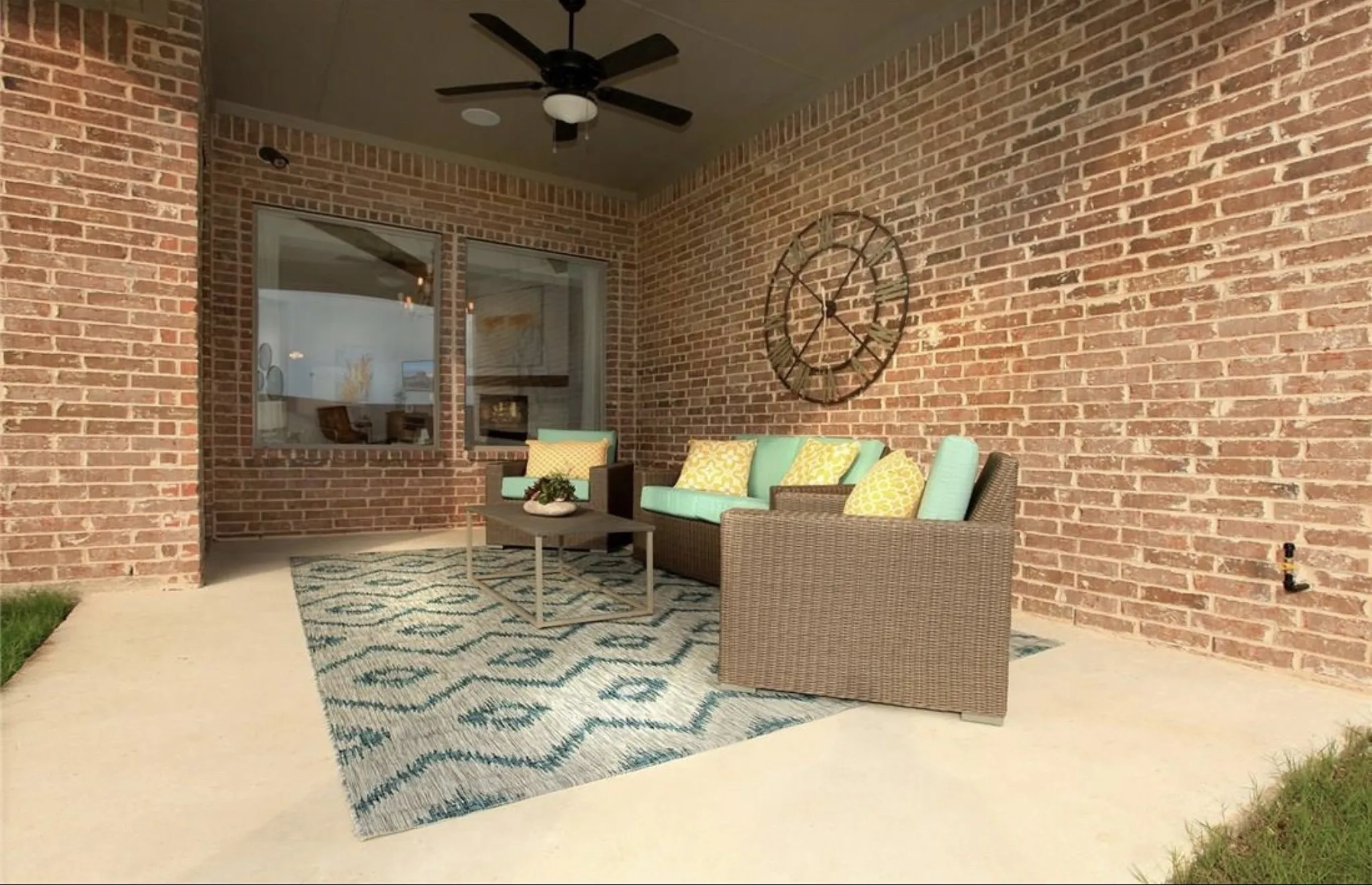 Covered patio retreat featuring exposed brick walls, ceiling fan, geometric patterned area rug, and wicker seating arrangement