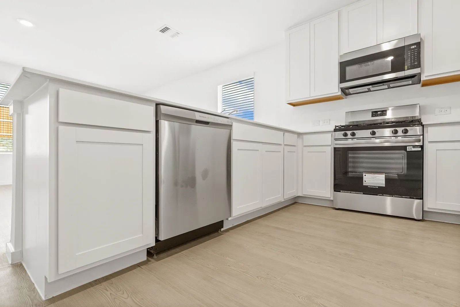 White kitchen cabinetry, stainless steel appliances, wood-finish flooring, and white countertops