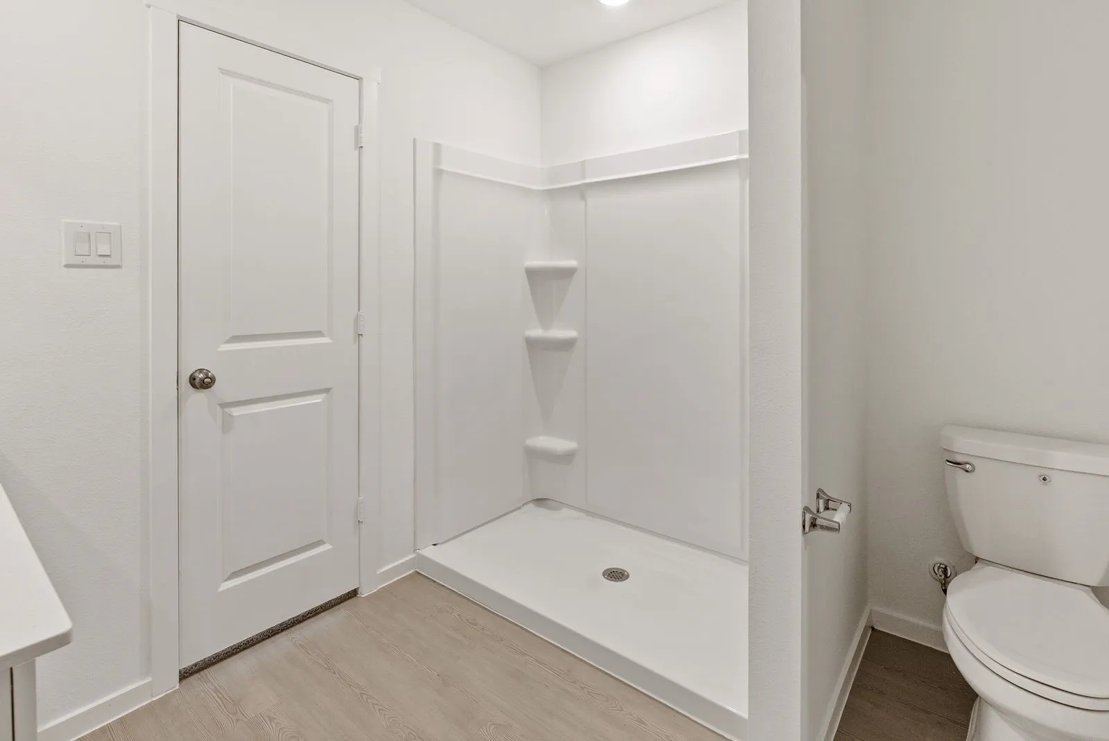 Walk-in shower with integrated shelving, commode, and wood-finish flooring