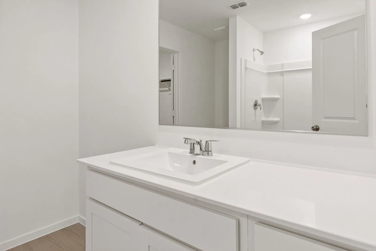 White vanity with an integrated sink and chrome faucet, set against a large wall-mounted mirror