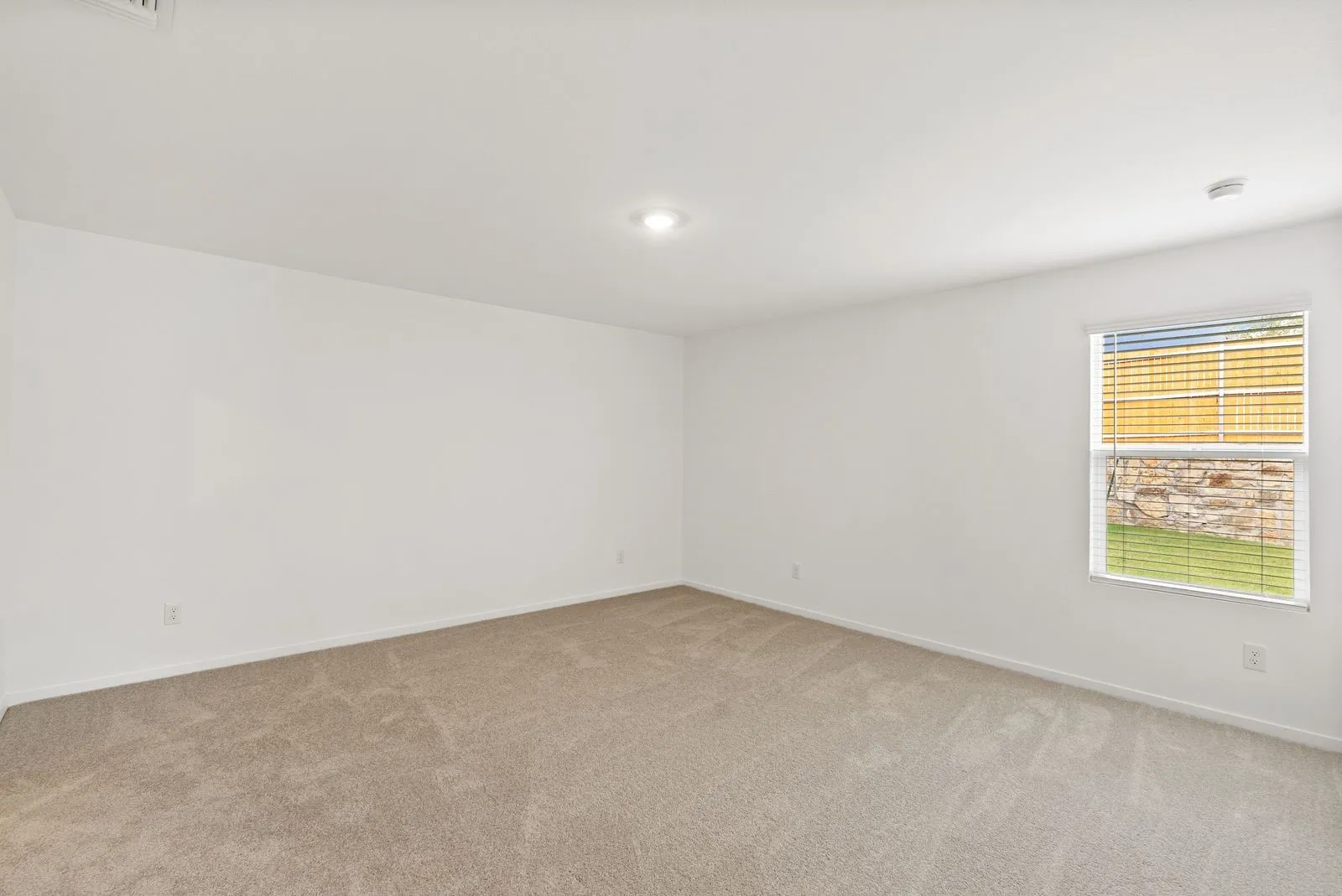 Neutral tone carpeting, white painted walls, recessed ceiling lighting, and a single window with blinds