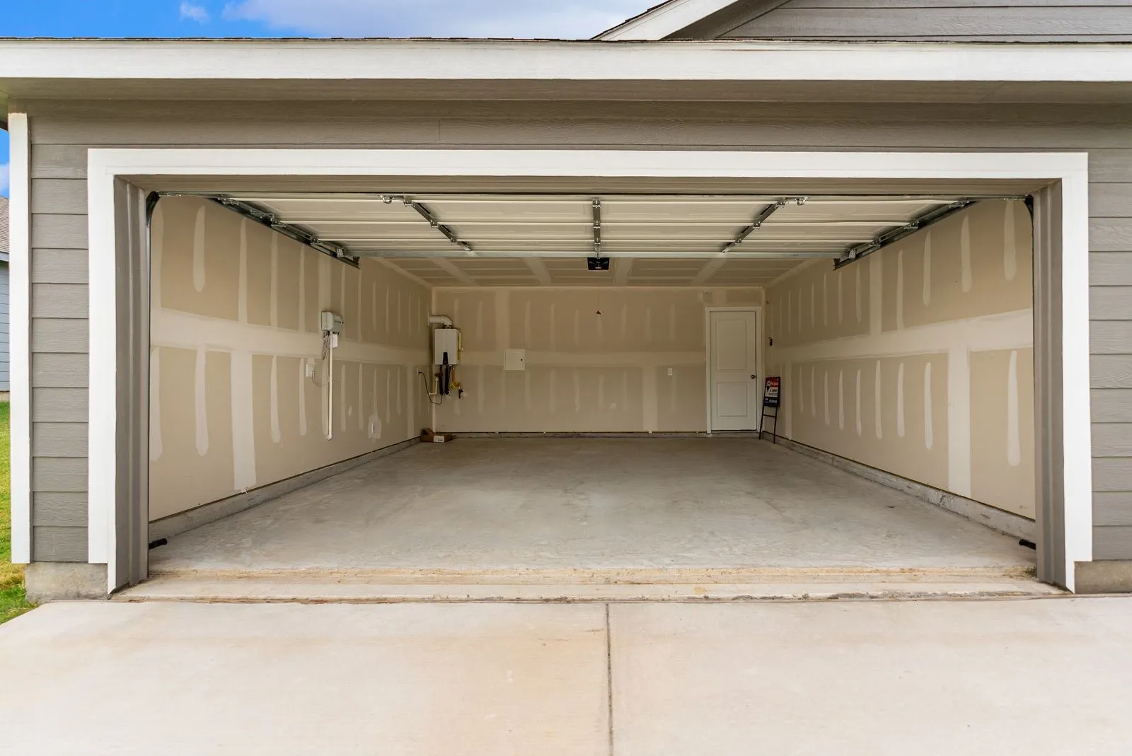Attached two-car garage with a concrete floor, finished walls, and a water heater