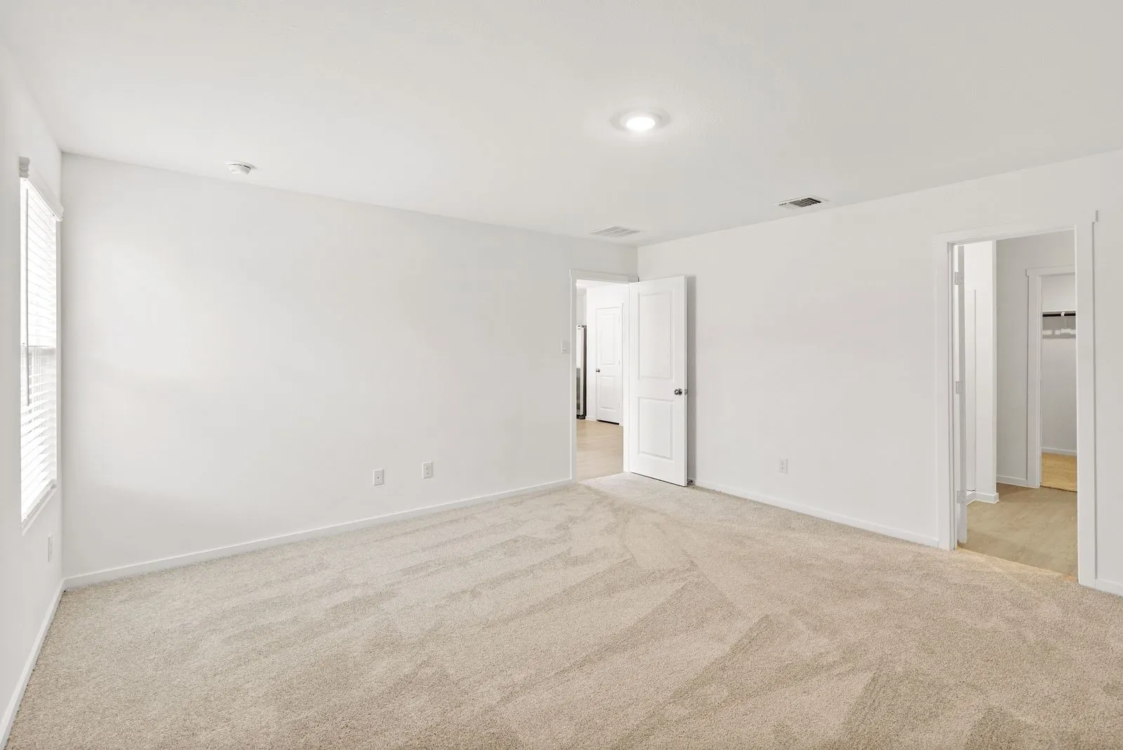 Spacious room featuring neutral carpeting, white walls, recessed lighting, and natural light from a window with blinds