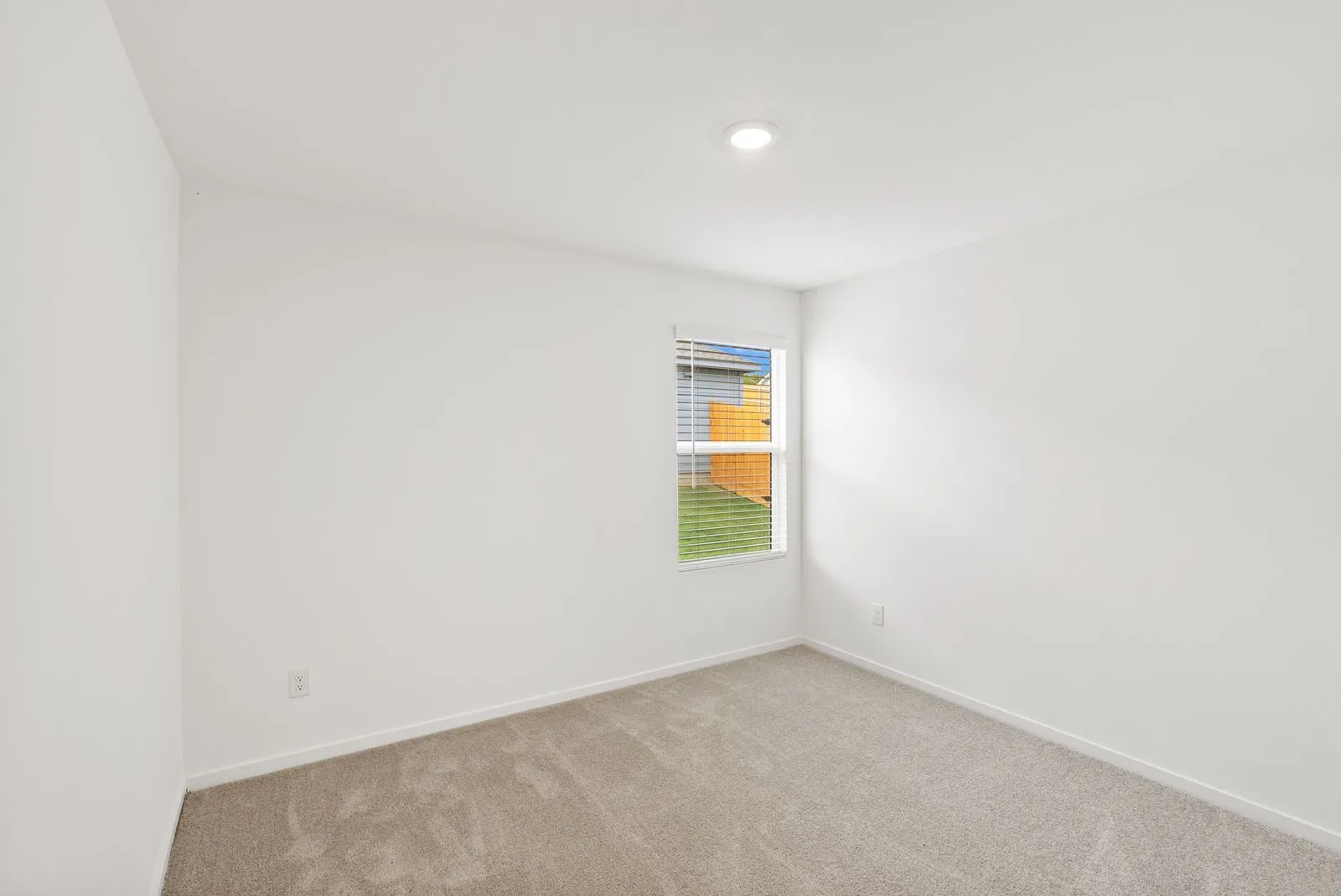 Recessed ceiling lighting, neutral carpeting, white wall finishes, and a double-hung window with blinds
