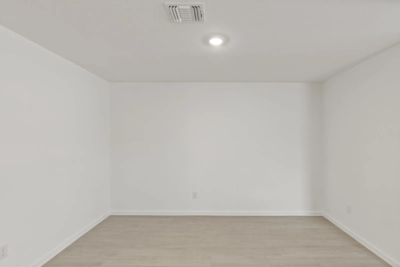 Recessed ceiling lighting illuminates a spacious room featuring light wood-finish flooring and neutral wall tones