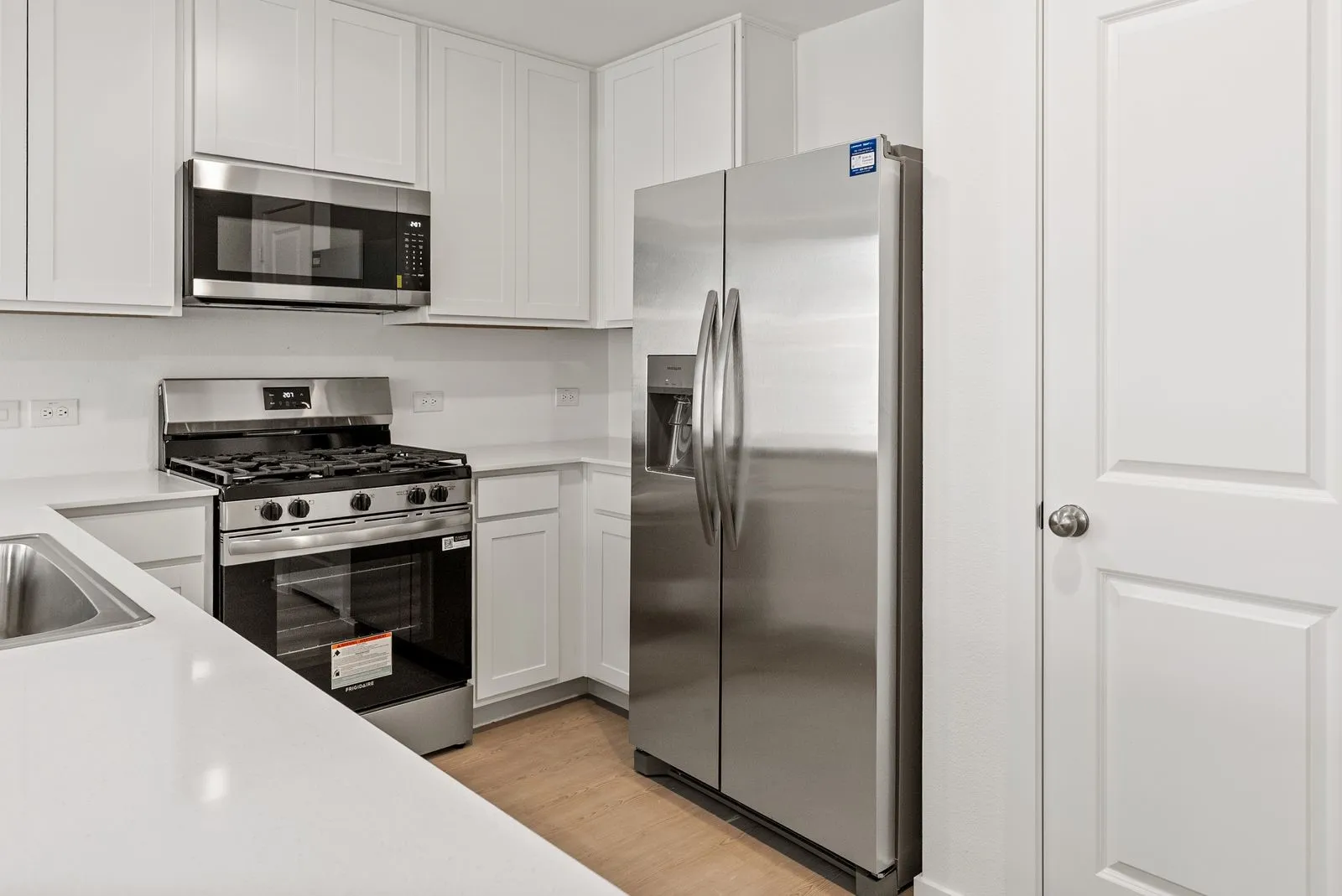 Kitchen featuring stainless steel appliances, white cabinetry, solid surface countertops, a built-in microwave, and wood-finish flooring