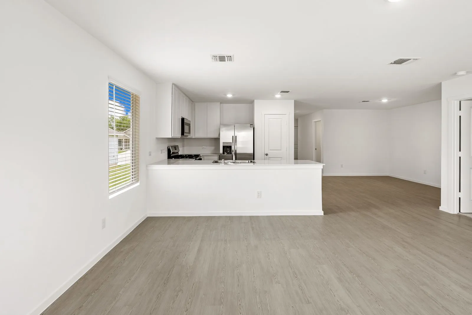 Open-concept layout featuring wood-finish flooring, recessed lighting, and a kitchen with light-colored cabinetry and stainless steel appliances