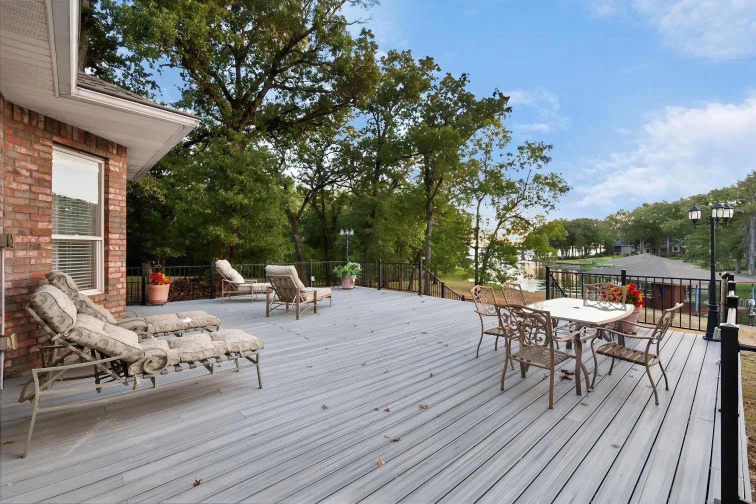 Expansive outdoor deck with composite decking, black metal railing, and mature trees, featuring a prominent lake backdrop