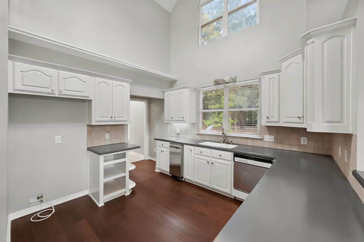 Kitchen featuring engineered hardwood flooring, white cabinetry, dark countertops, and a stainless steel dishwasher and an ice maker