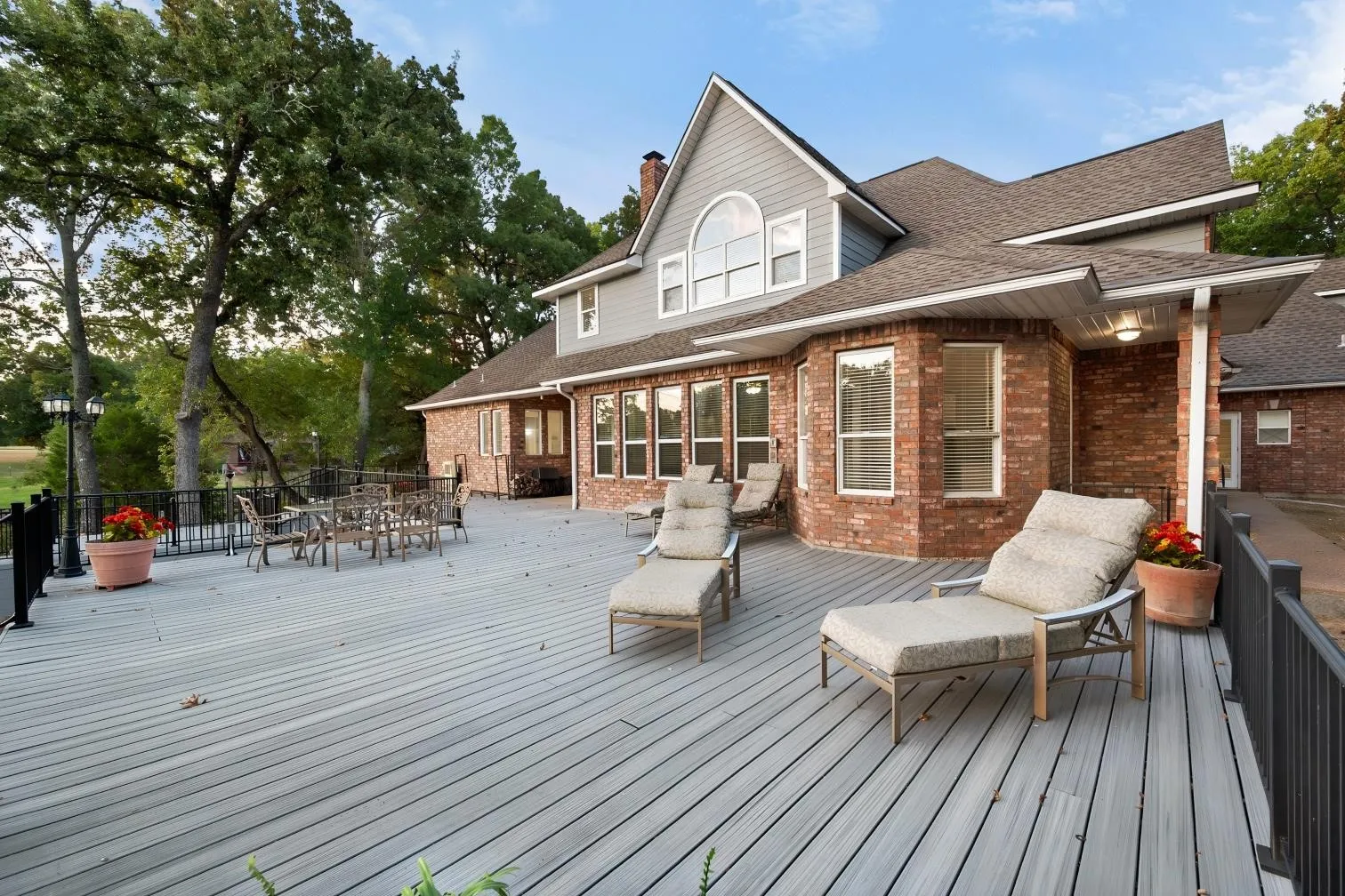 Expansive outdoor deck with composite decking, brick and siding exterior, multiple windows, and exterior lighting fixtures