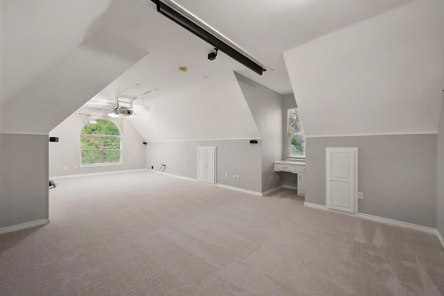 Spacious room with sloped ceilings, light-toned carpeting, a built-in desk, and an arched window, featuring a projection system for your home movies