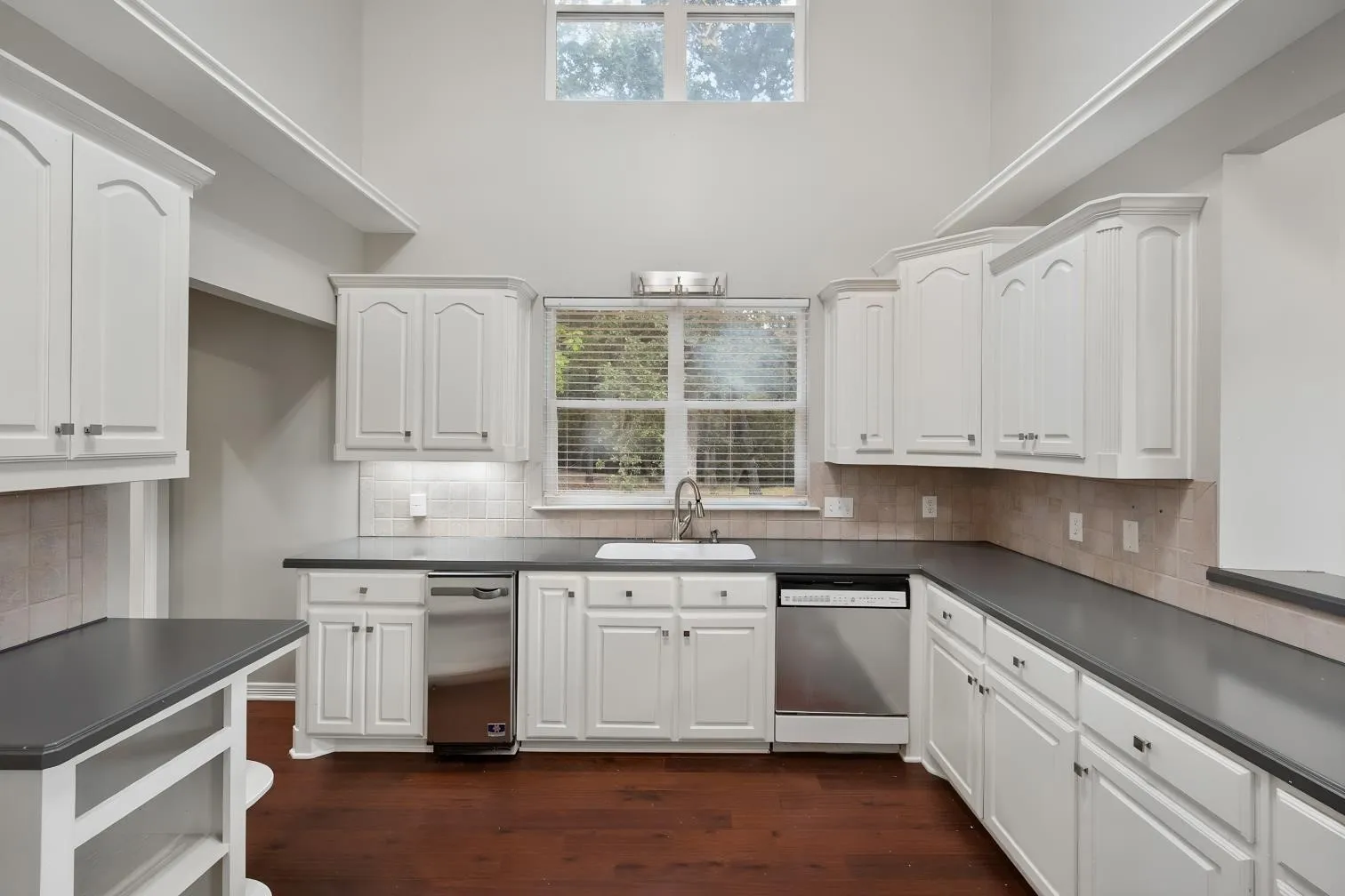 Kitchen featuring extensive white cabinetry with brushed nickel hardware, dark countertops, a stainless steel dishwasher, and a white undermount sink