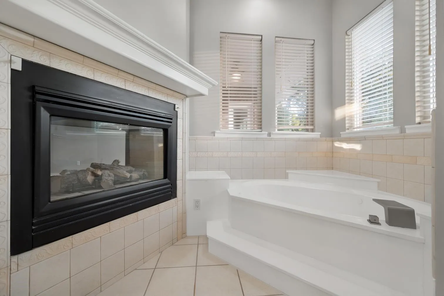 Built-in see through fireplace with a tile surround and mantel accenting a jetted tub