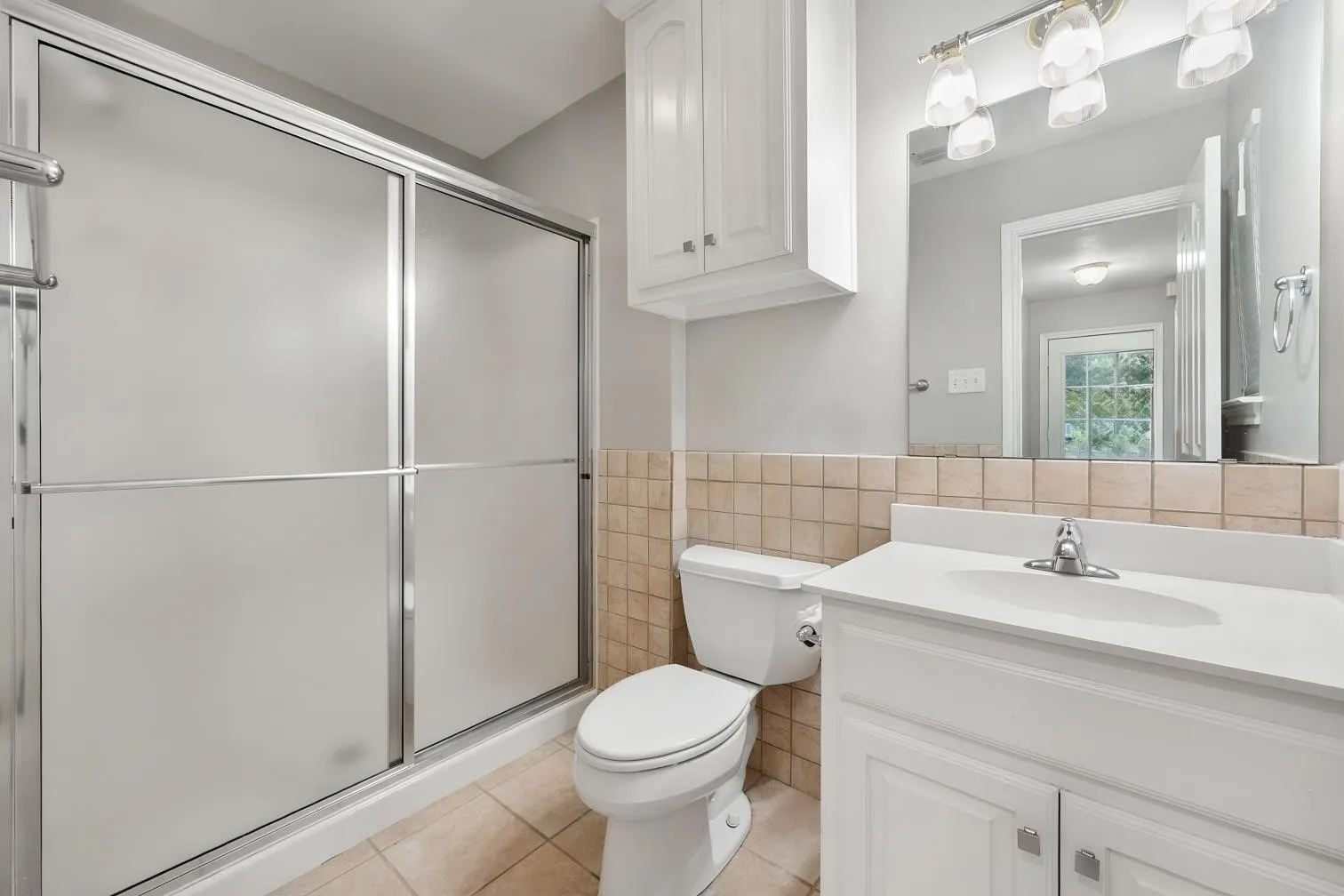 Frosted glass shower enclosure, white vanity with integrated sink, coordinating wall-mounted storage cabinet, and tile flooring