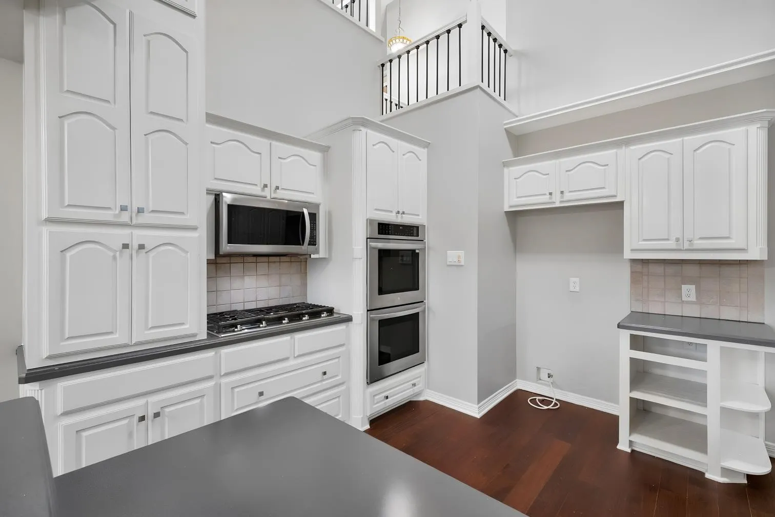 White cabinetry with brushed nickel hardware, stainless steel appliances, tile backsplash, dark engineered hardwood flooring, and a view of the second story