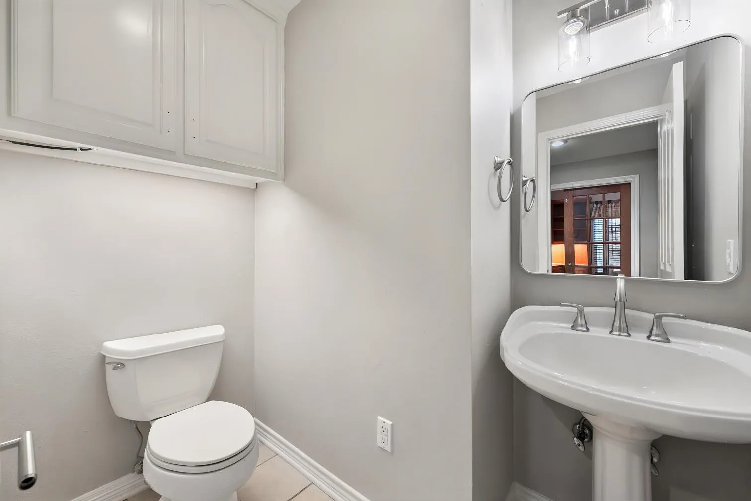 Pedestal sink with brushed nickel faucet, wall-mounted mirror, overhead lighting, and built-in white cabinetry