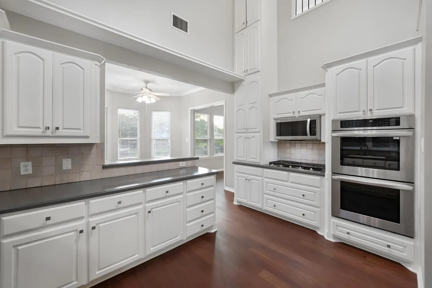 Kitchen featuring white cabinetry, dark countertops, engineered hardwood flooring, and built-in stainless steel appliances