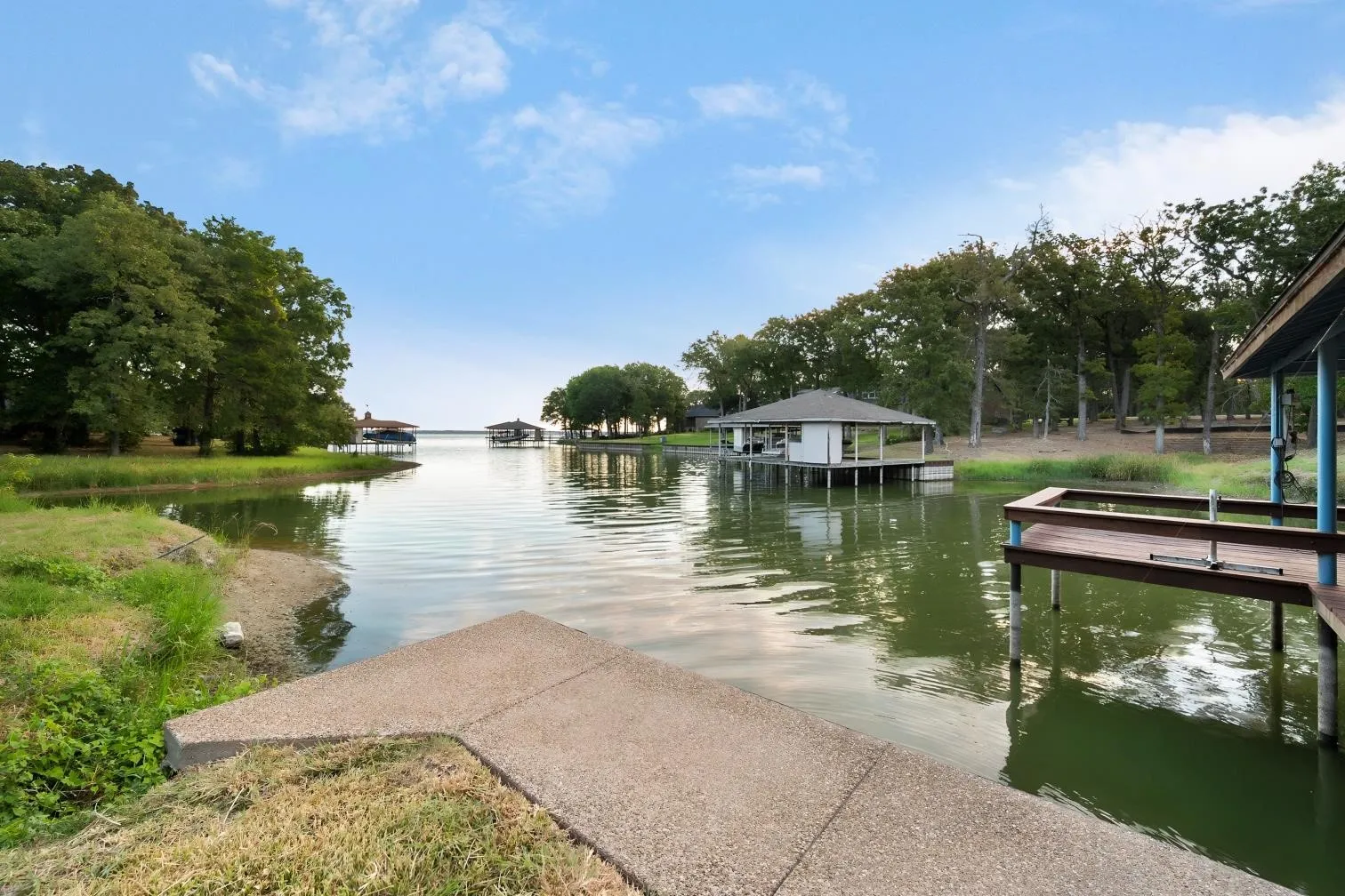 Waterfront property featuring a concrete sidewalk, a wooden dock, and a covered boat slip