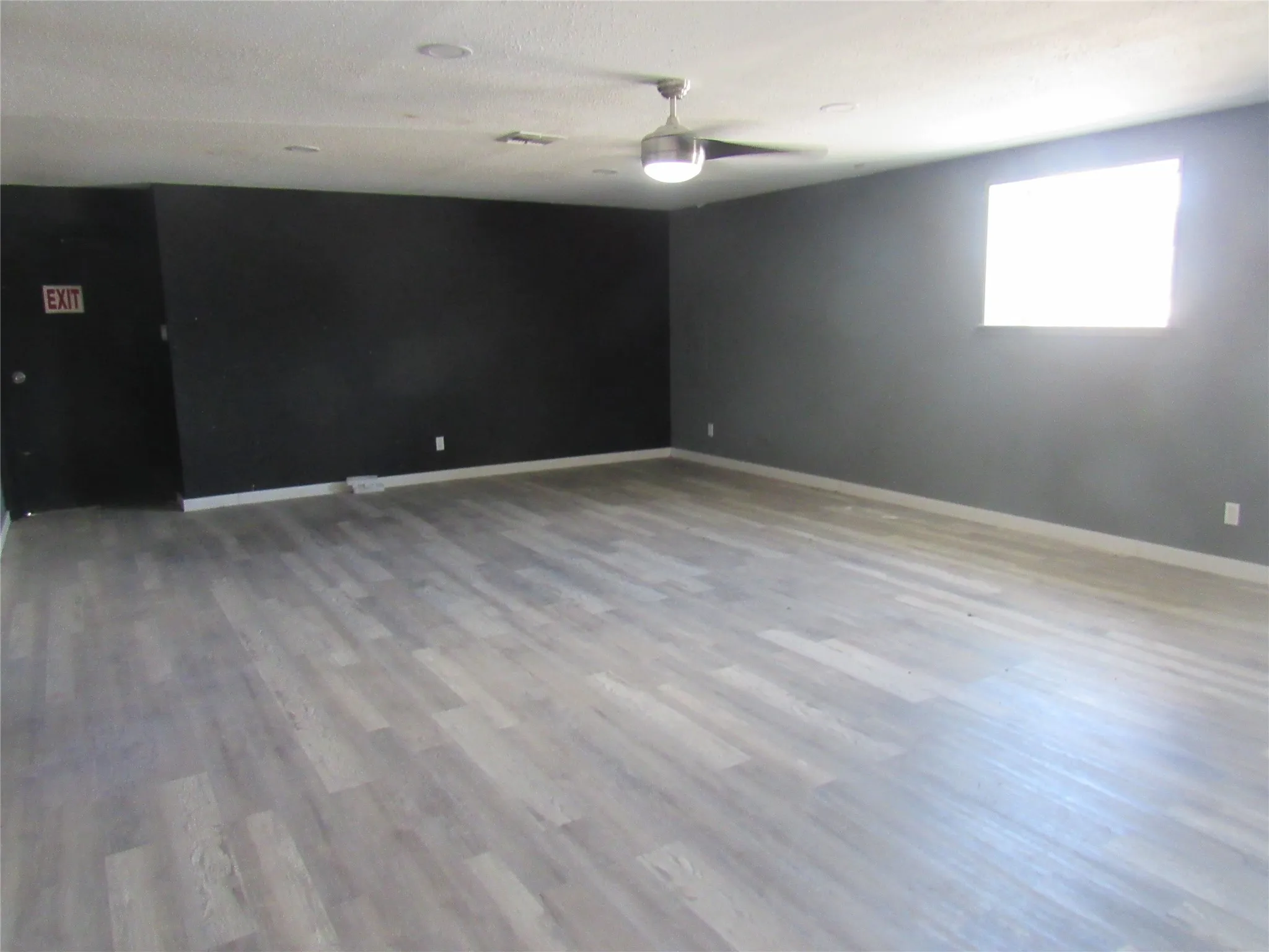Expansive room featuring wood-finish flooring, a ceiling fan, recessed lighting, and a window for natural illumination