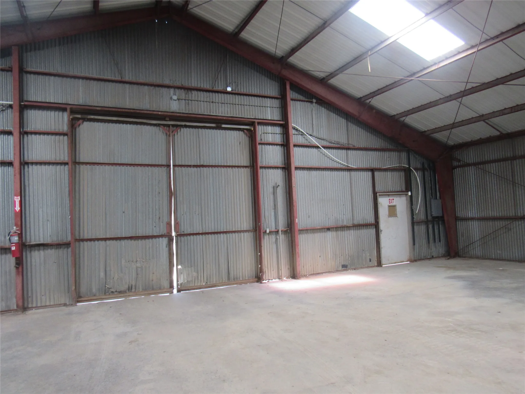 Metal construction with exposed structural beams, a large sliding bay door, concrete flooring, and a skylight