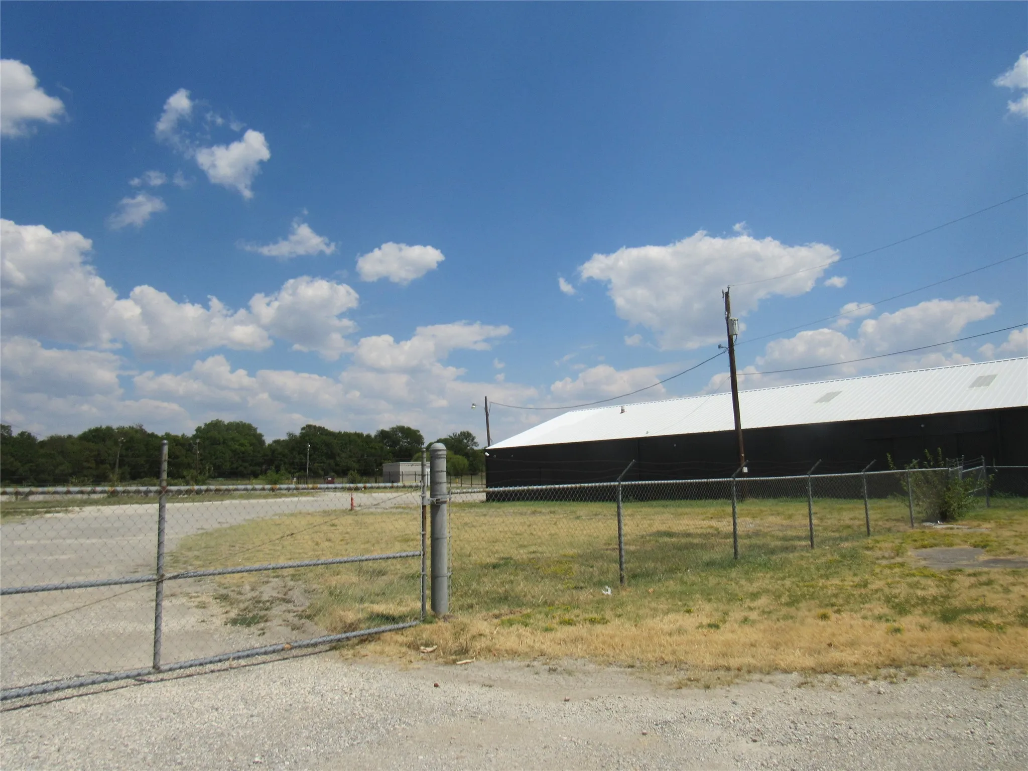 Chain-link perimeter fencing with a gated entry, expansive gravel lot, and a large structure with a metal roof