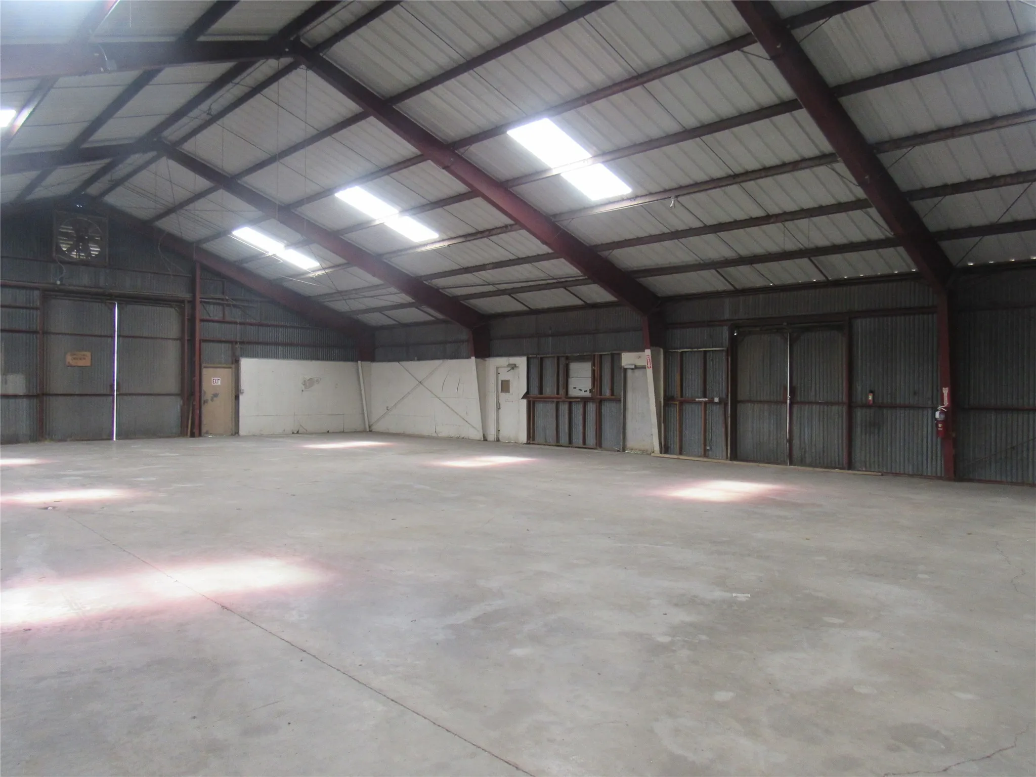 Expansive interior space featuring a concrete floor, high vaulted ceiling with exposed metal beams, and overhead skylights