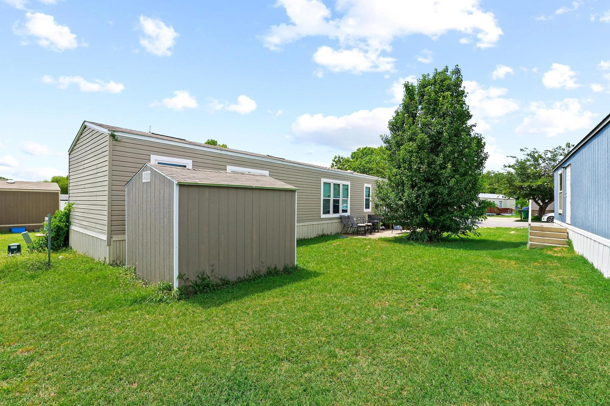 Expansive grassy yard featuring a mature tree, a private patio area, and a detached storage shed
