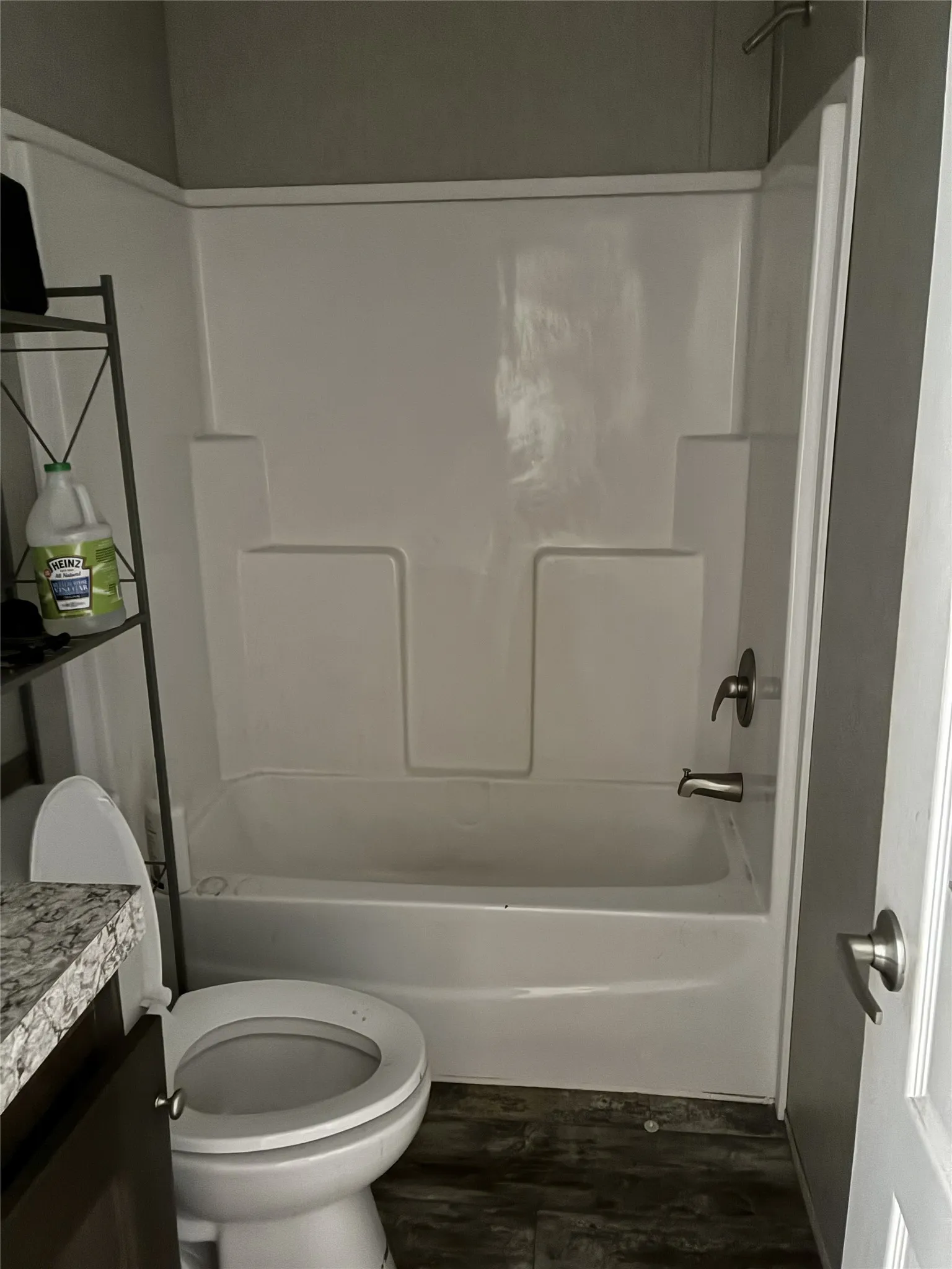 Bathtub with shower, toilet, and wood-finish flooring