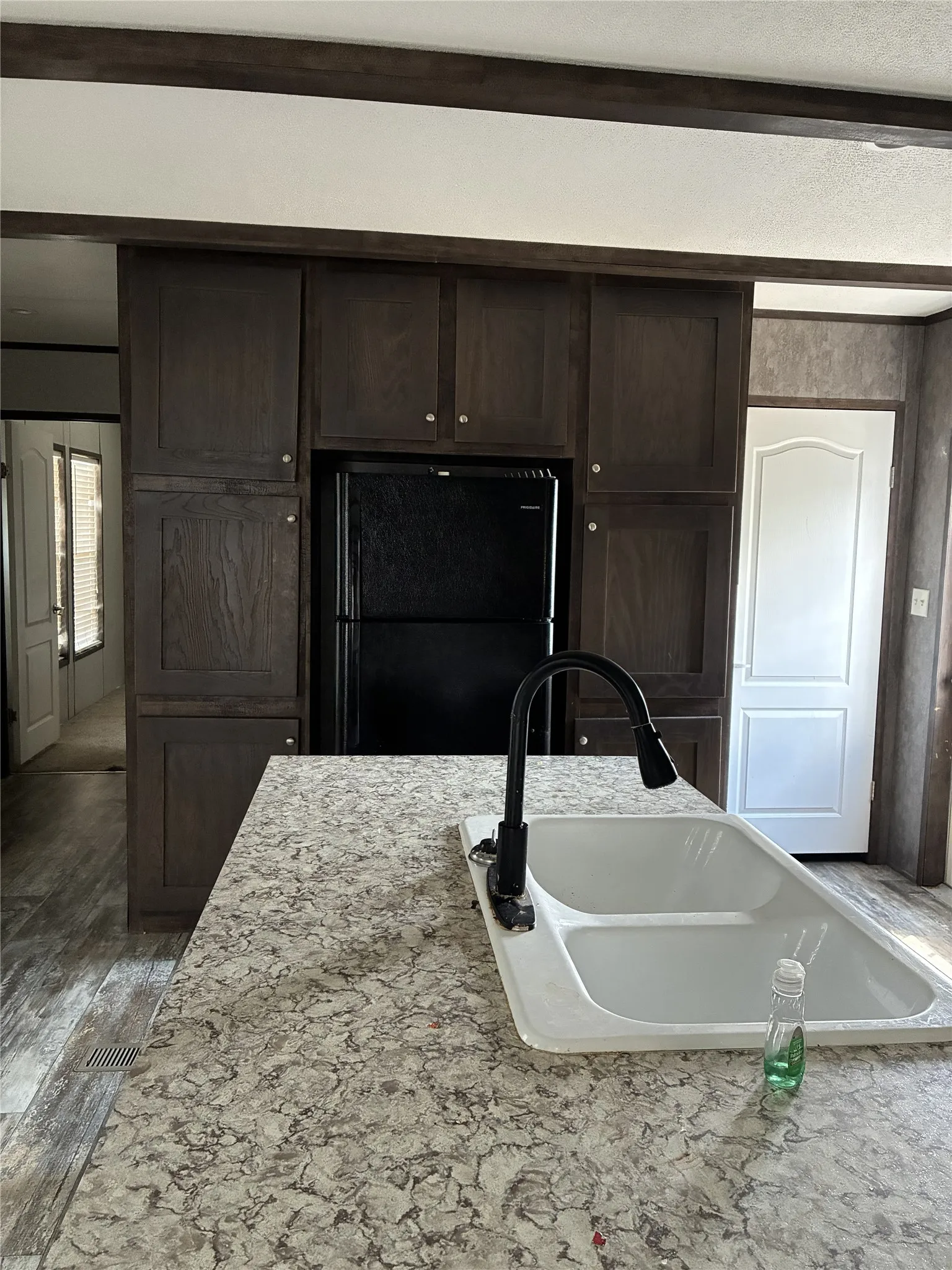 Kitchen island featuring a double basin sink with a matte black high-arc faucet, patterned countertop, and wood-finish flooring