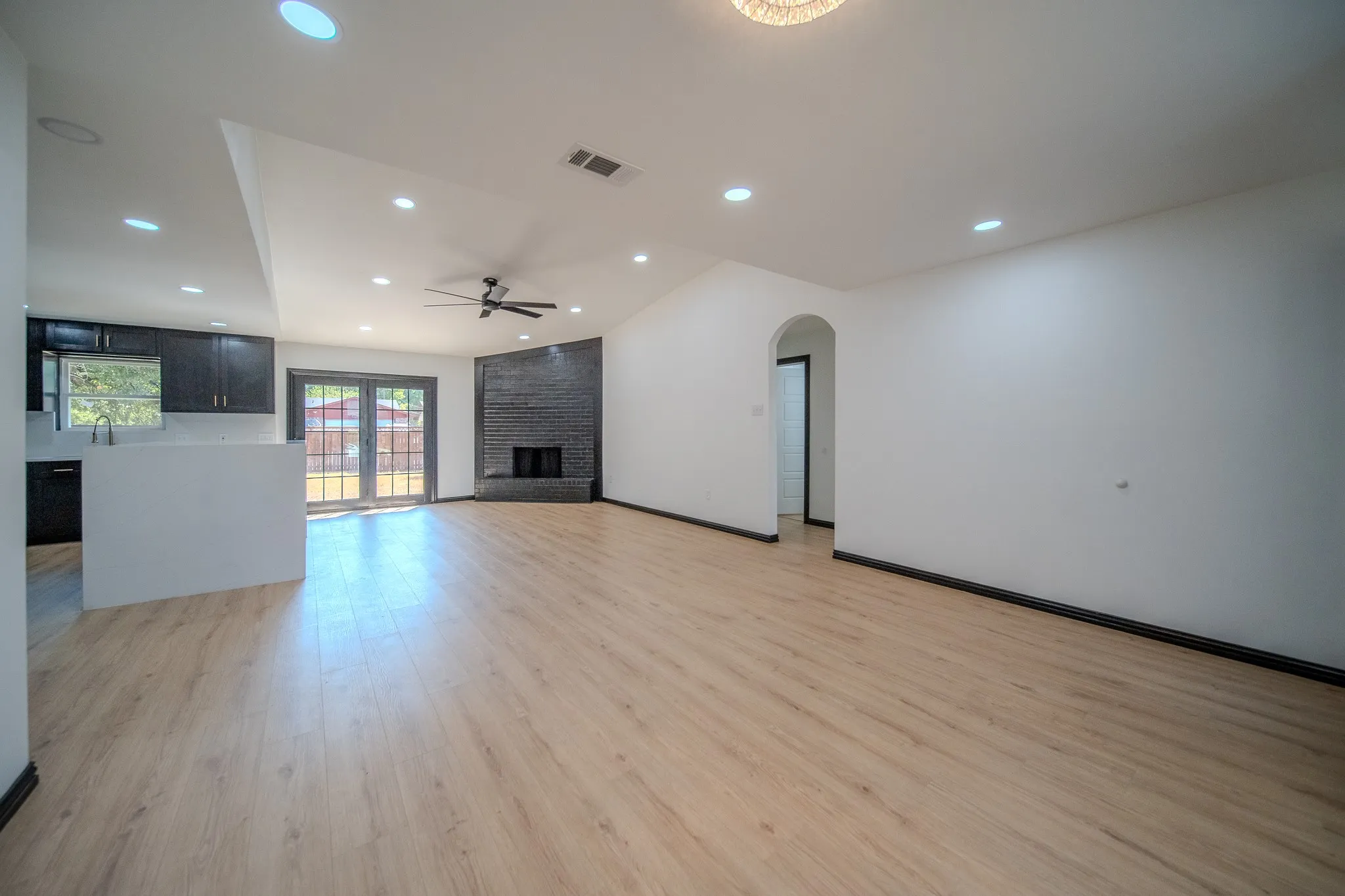 Vaulted ceilings with recessed lighting, wood-finish flooring, a black brick fireplace, and an arched doorway