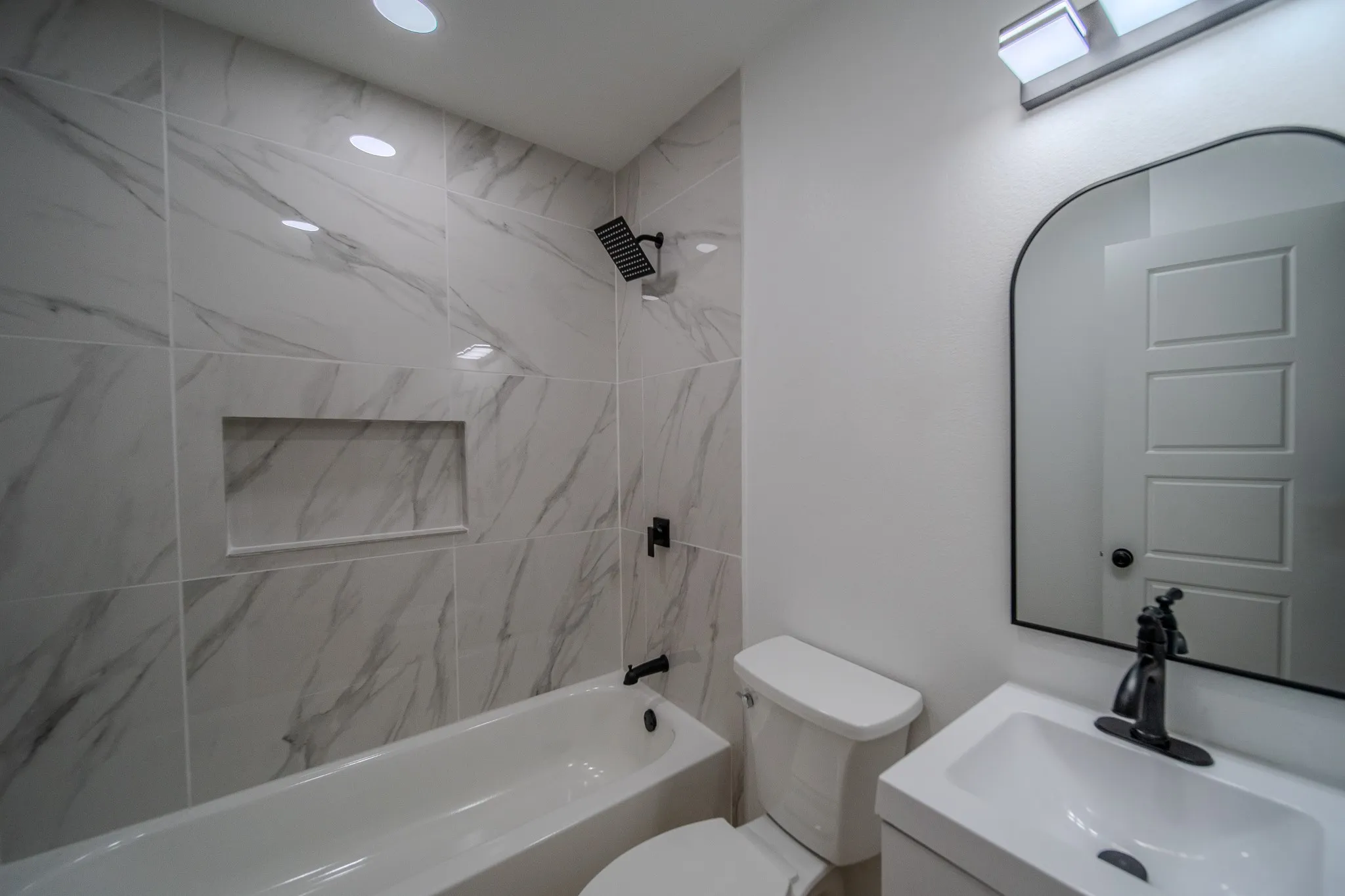 Tub/shower combination with marble-look tile surround, recessed shower niche, and matte black fixtures