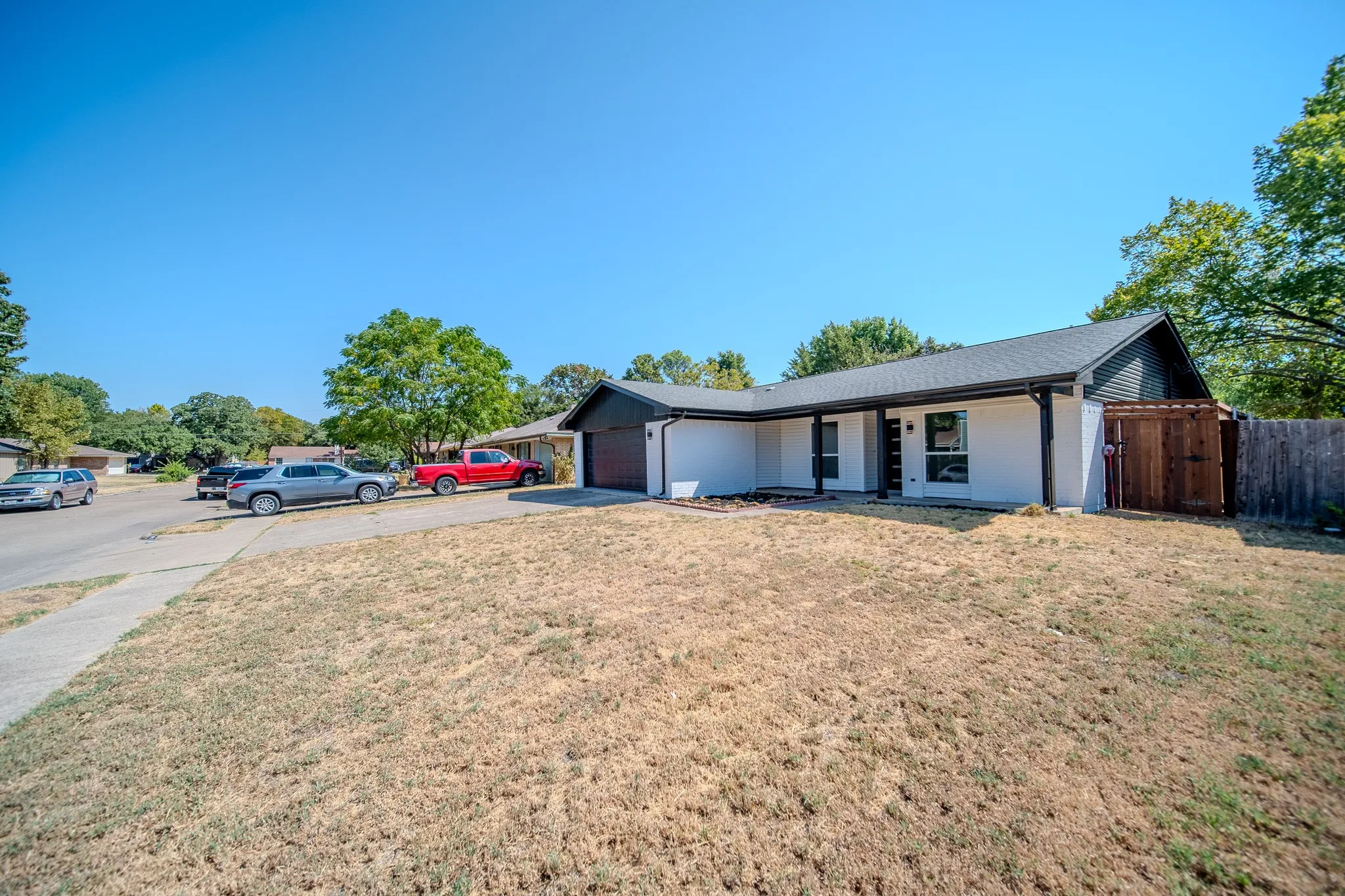 Single-story exterior with white siding and dark trim accents, featuring a covered porch entry, an attached garage, and a wood privacy fence