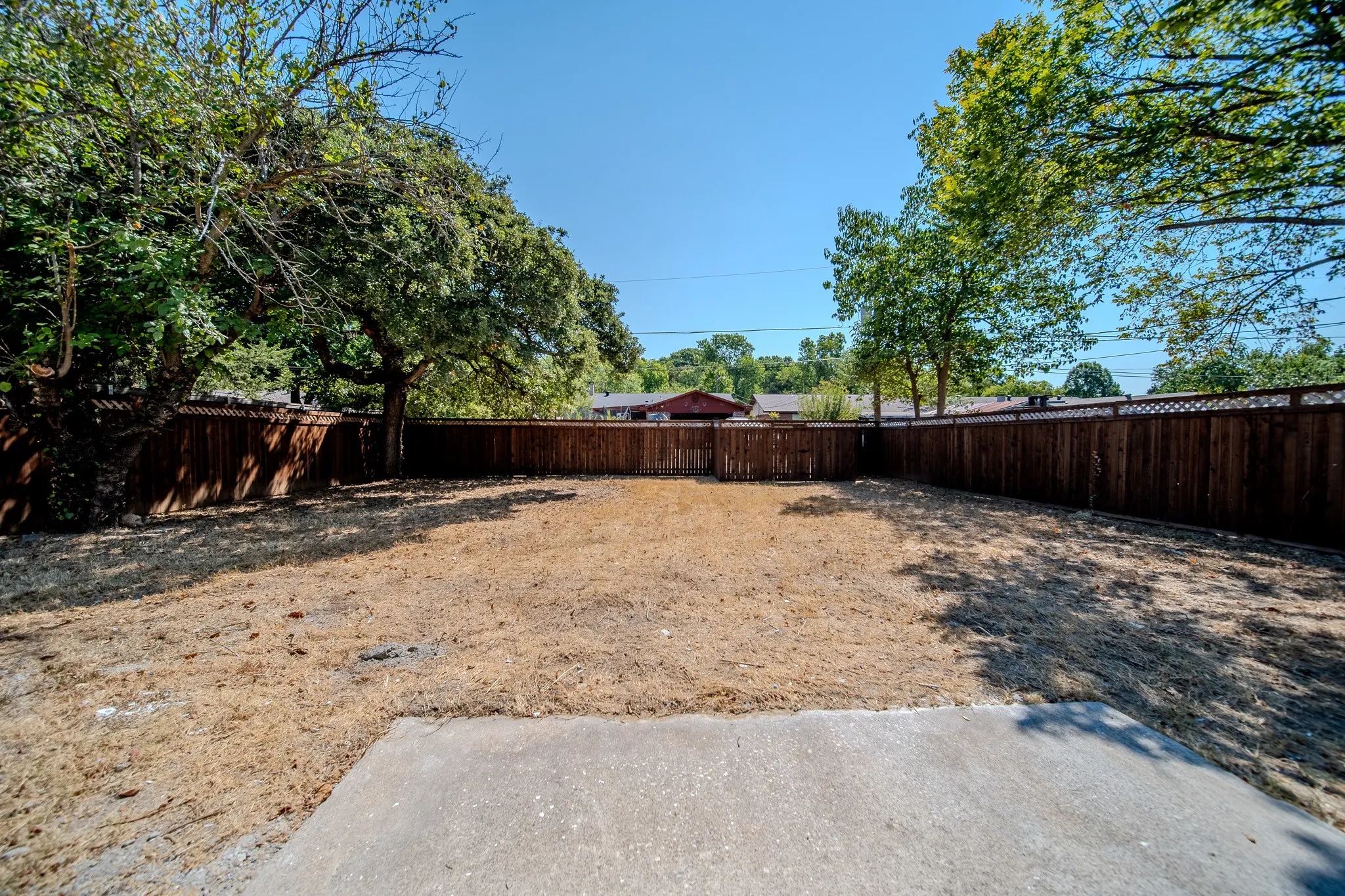 Spacious backyard with a perimeter wood fence, mature trees, and a concrete patio pad