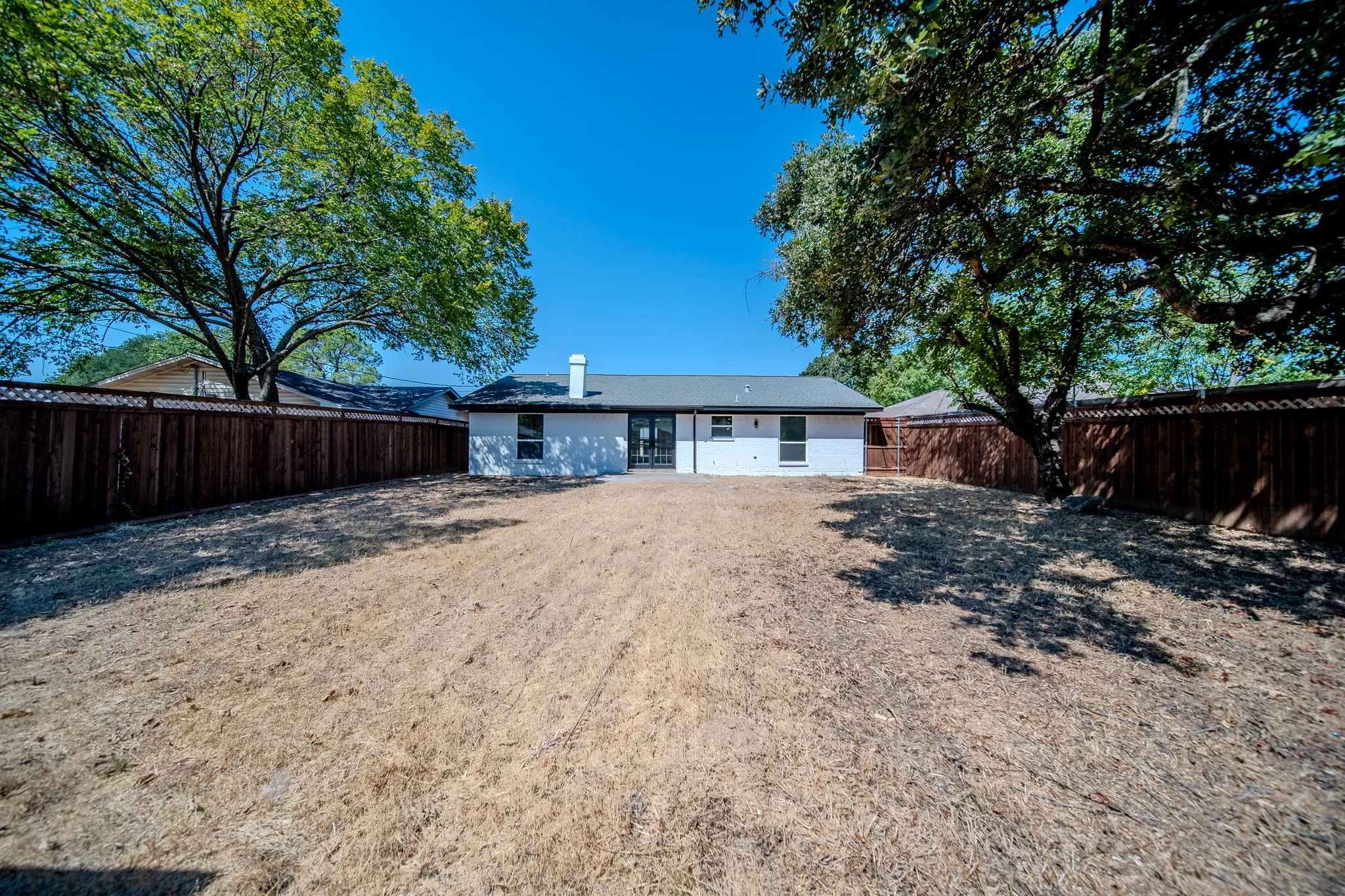 Expansive backyard with a wood privacy fence, mature trees, and a white stucco exterior