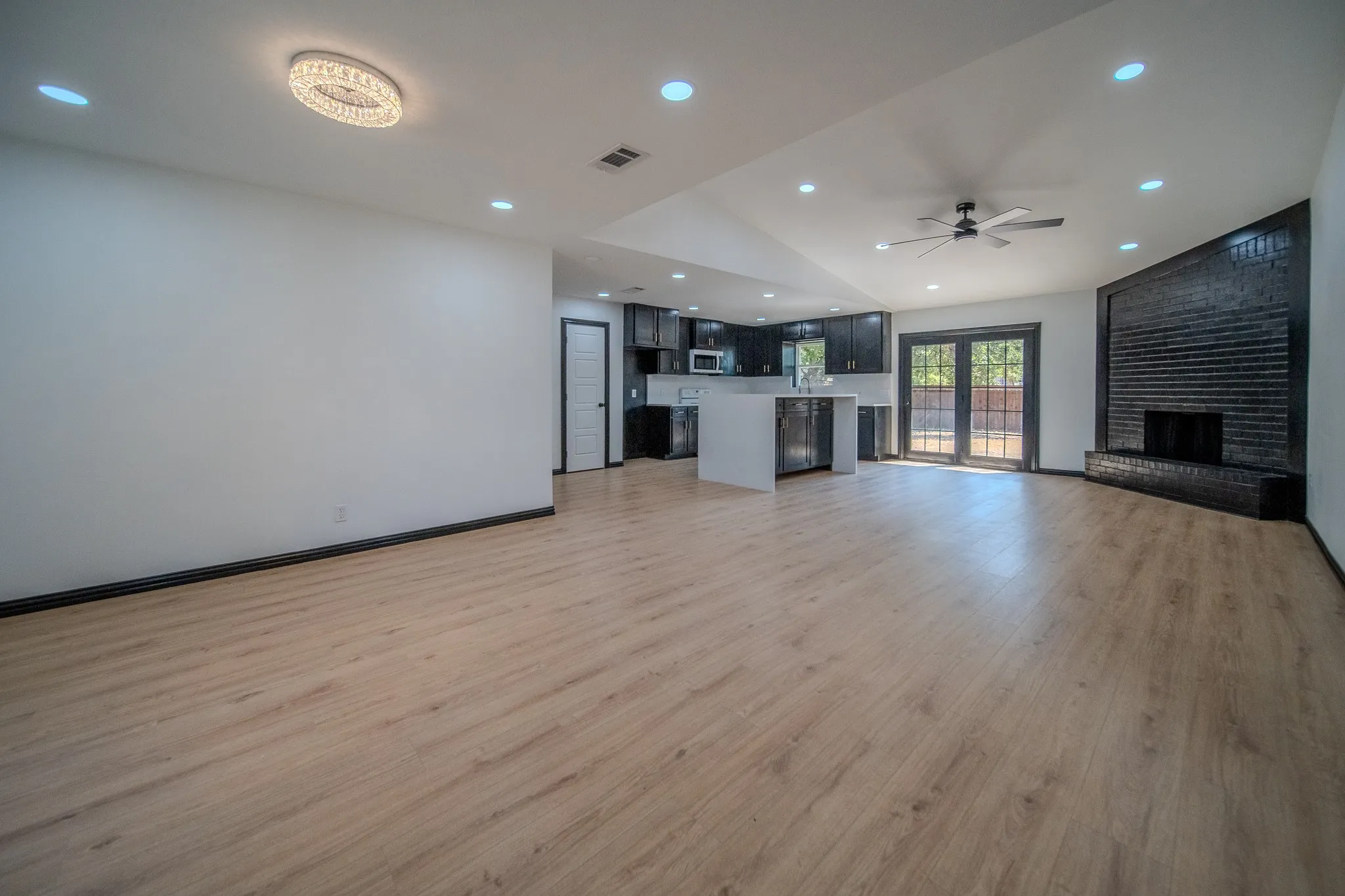 Wood-finish flooring throughout, recessed lighting, vaulted ceiling, black brick fireplace, and French doors