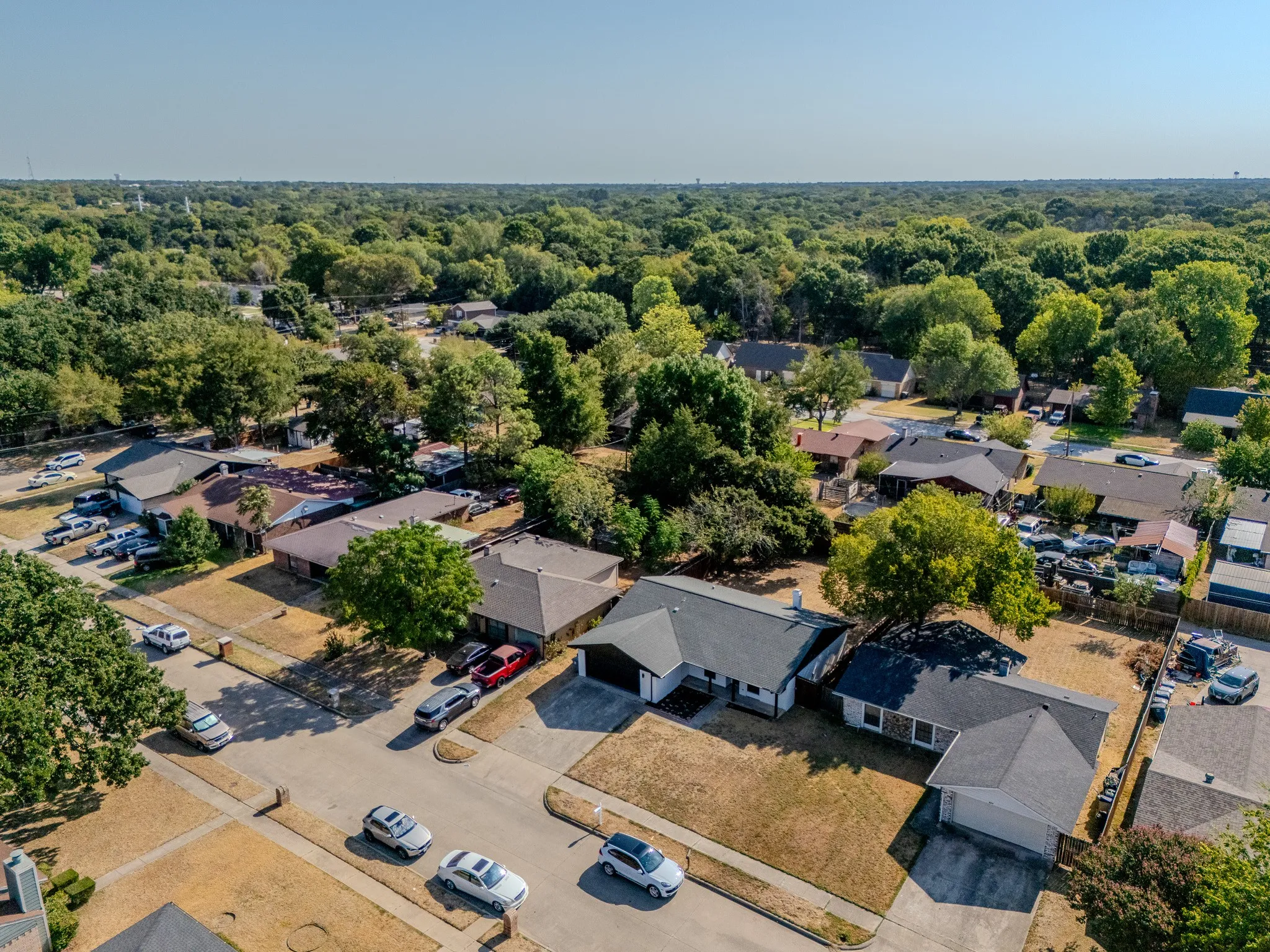 Residential street featuring single-story homes with dark shingle roofs, attached garages, and mature trees throughout the neighborhood