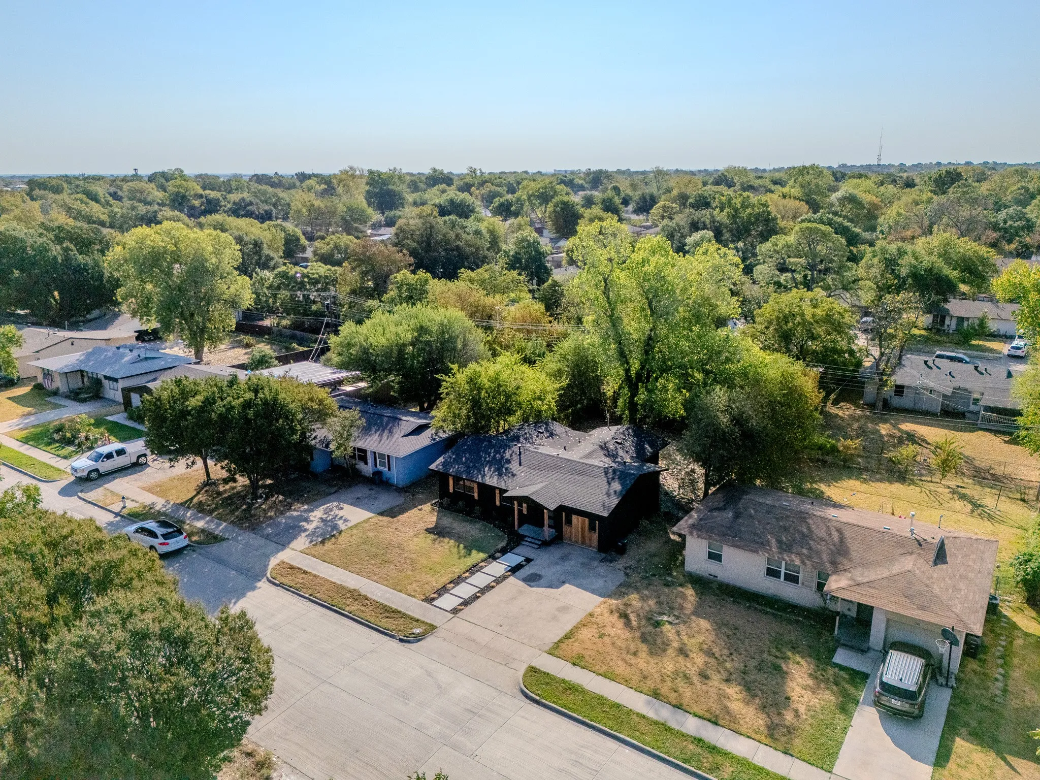 Residential property with a dark-pitched roof, mature trees, and concrete driveway