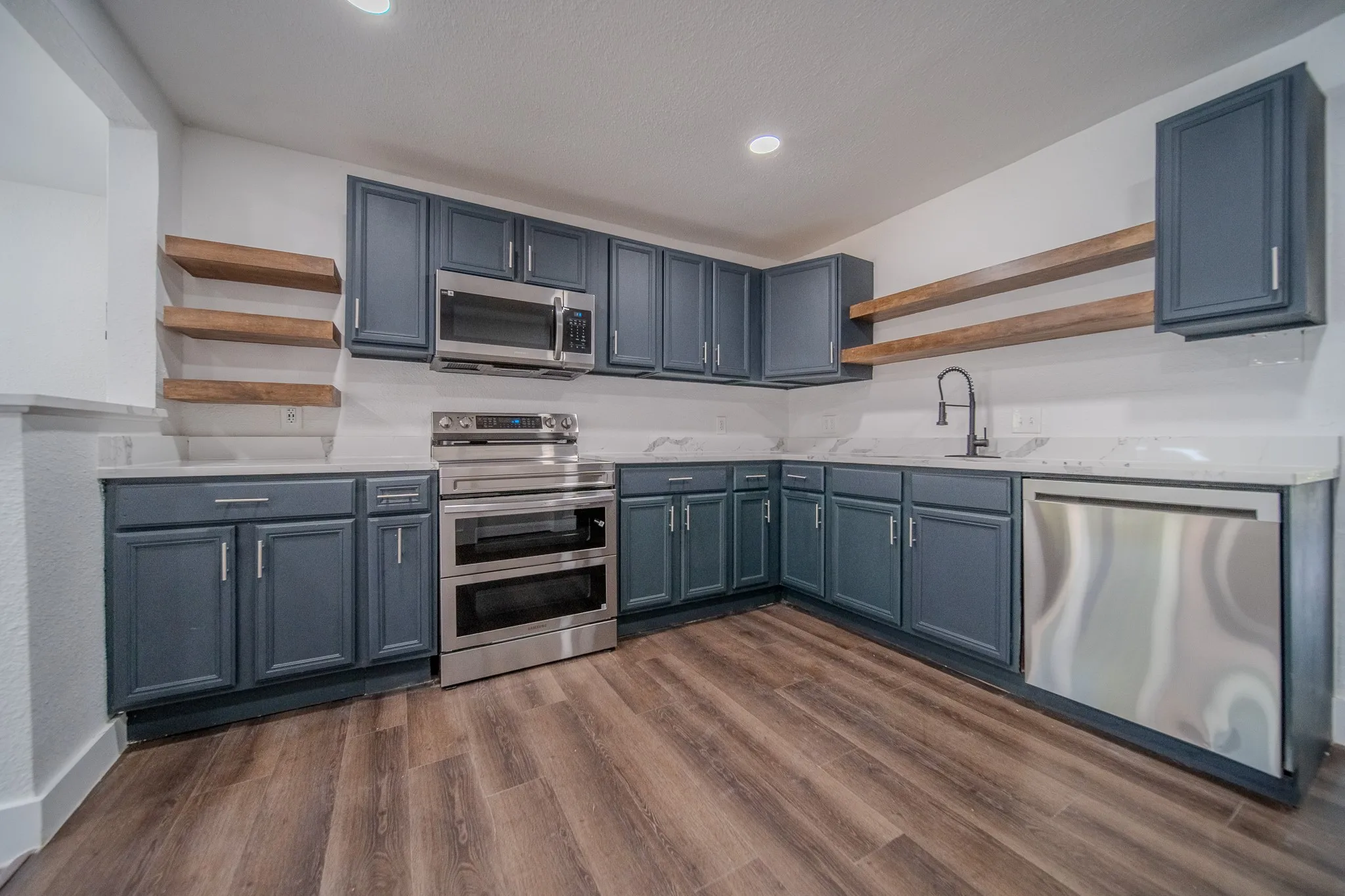 Modern kitchen featuring navy cabinetry, stainless steel appliances, stone countertops, and wood-finish flooring
