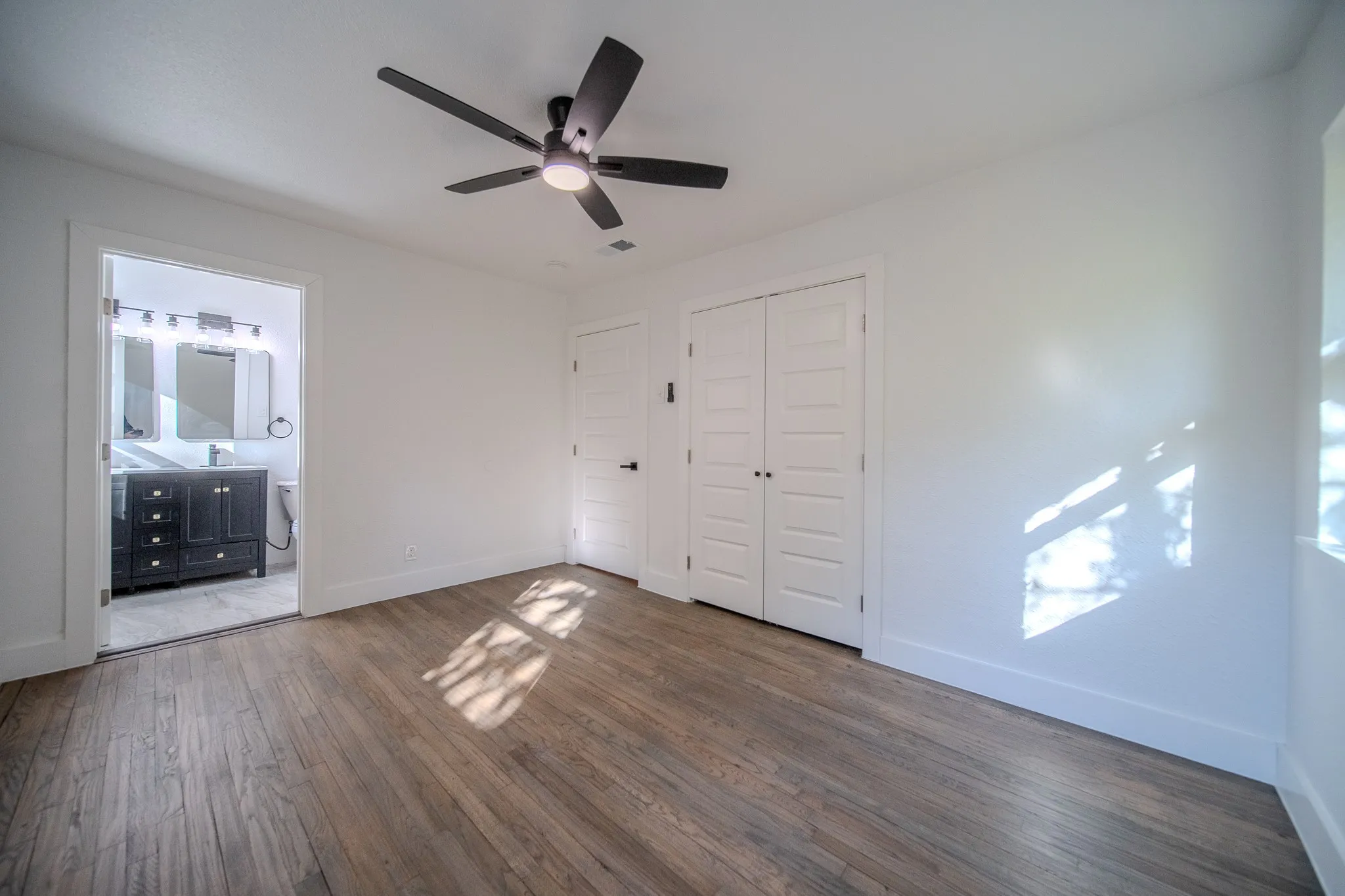 Wood-finish flooring, a ceiling fan with integrated lighting, and white walls