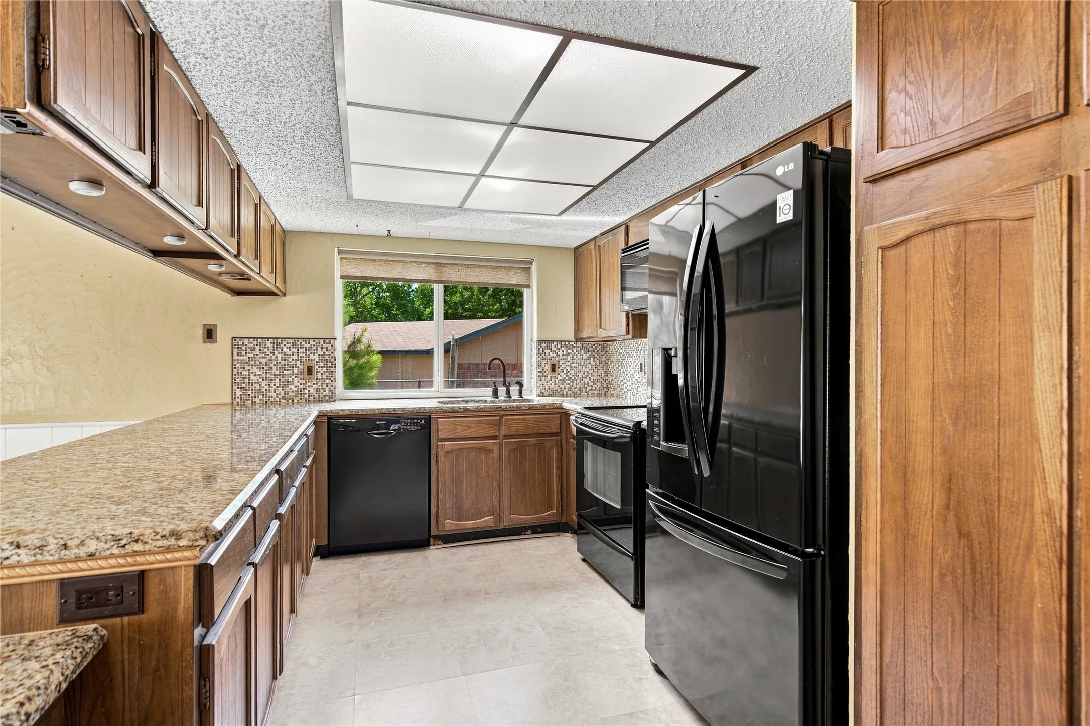 Kitchen featuring wood cabinetry, granite countertops, tile backsplash, and black appliances