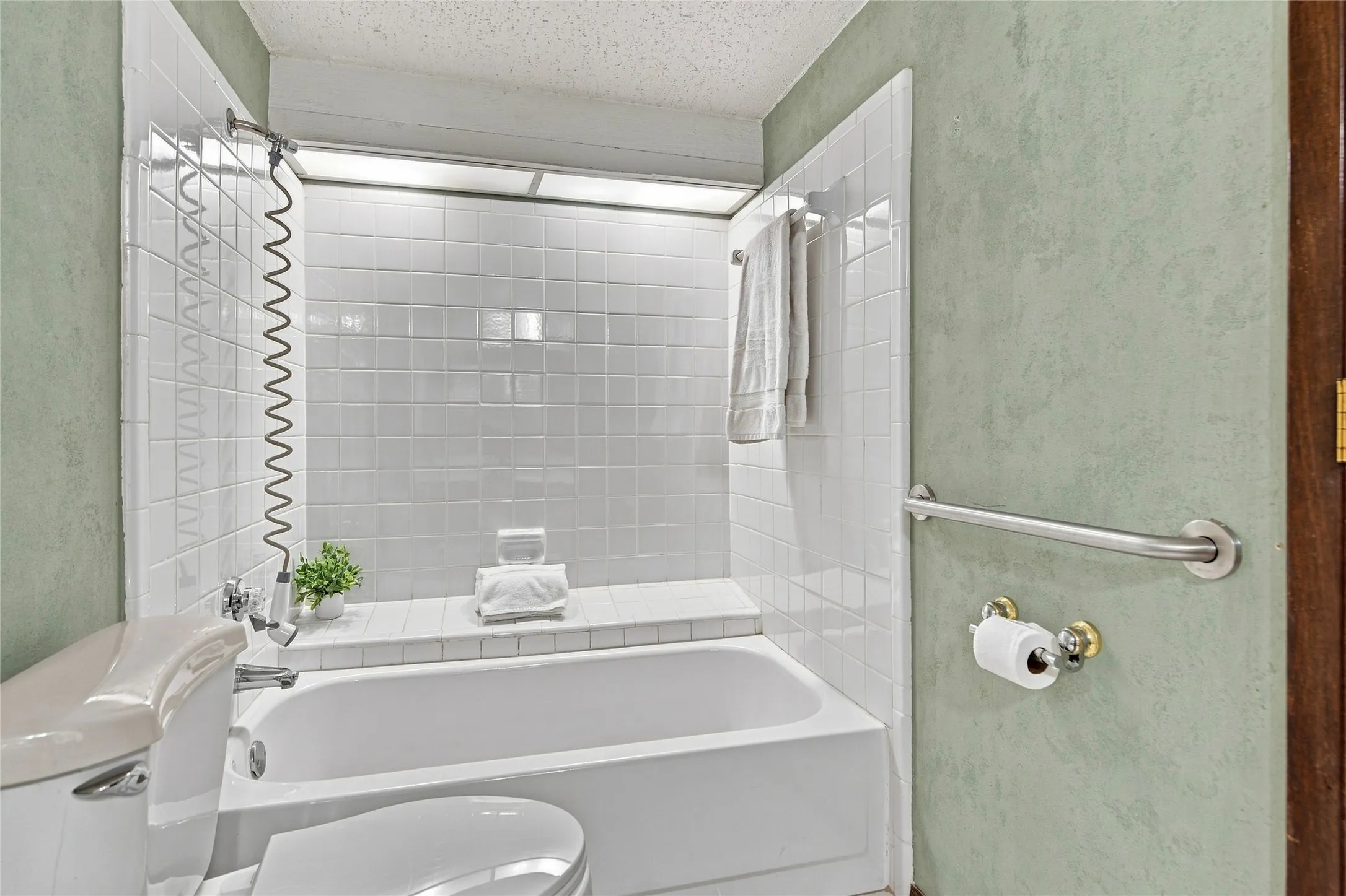 Clean and functional bathroom featuring a white subway tile shower surround with glass enclosure, integrated bathtub, chrome fixtures, and soft green wall finishes