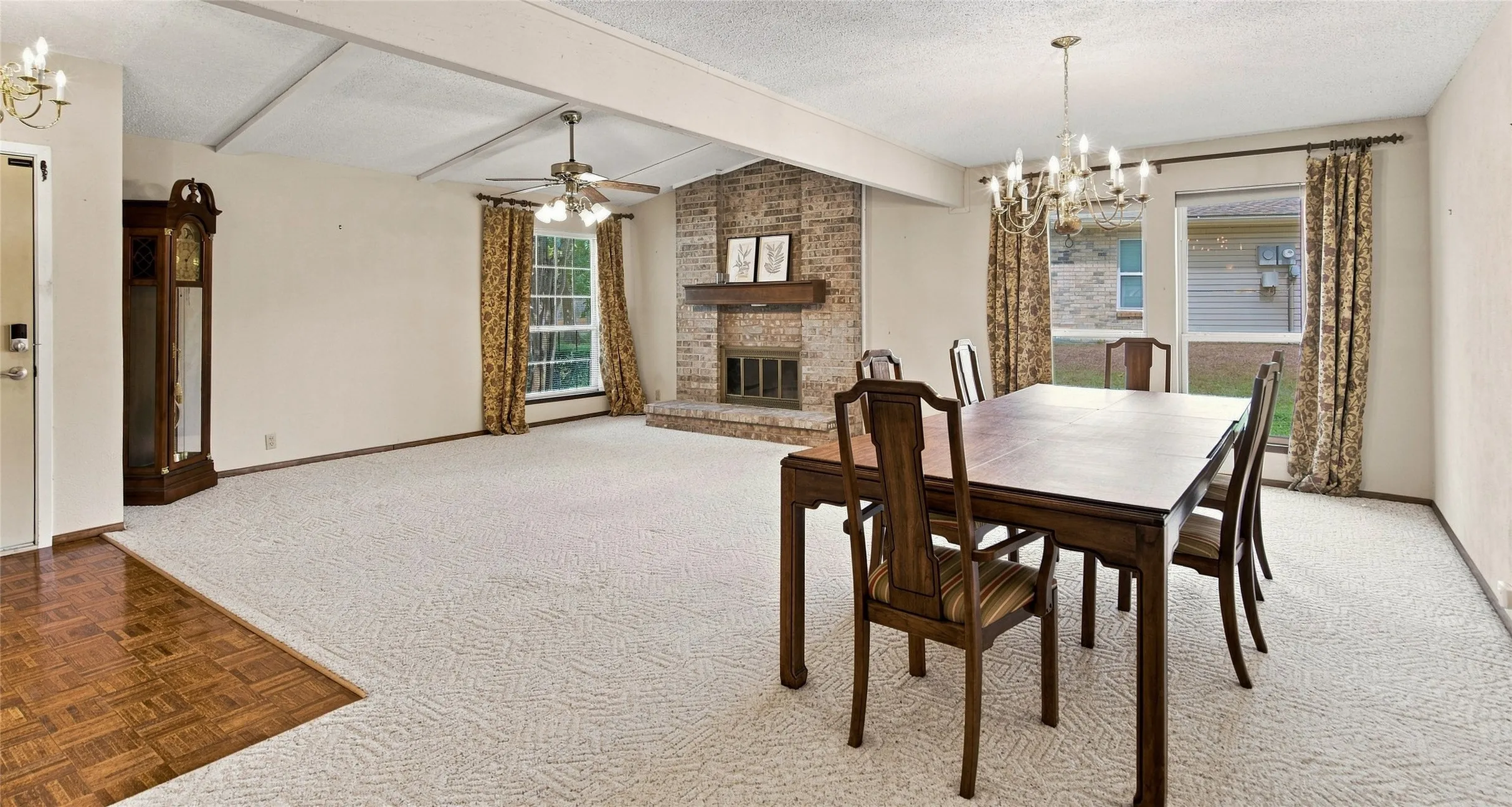 Spacious living area featuring a brick fireplace, tray ceiling with exposed beams, ceiling fan, and large windows