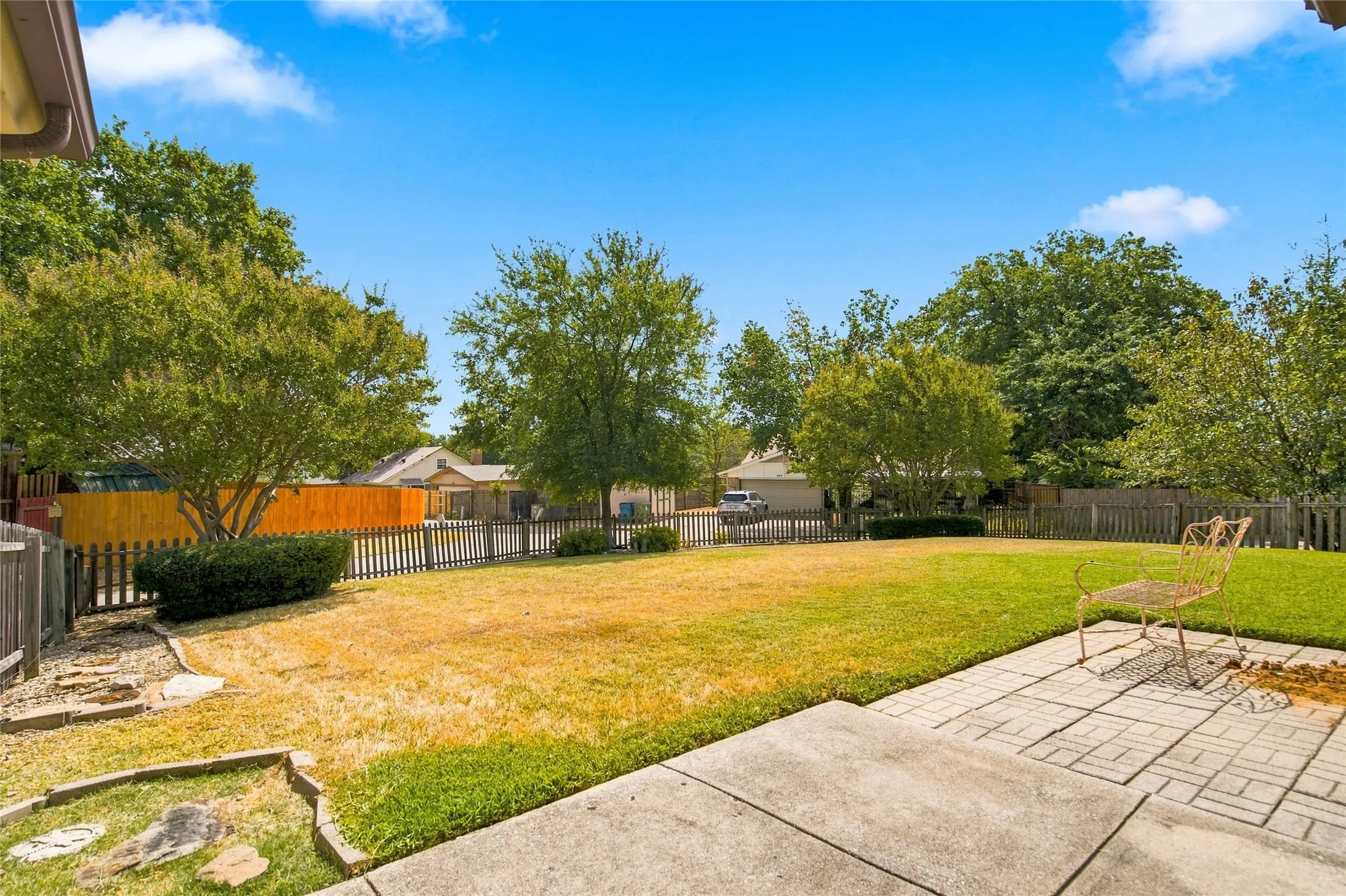 Expansive lawn area with mature trees, bordered by a wood fence, and featuring a paver patio